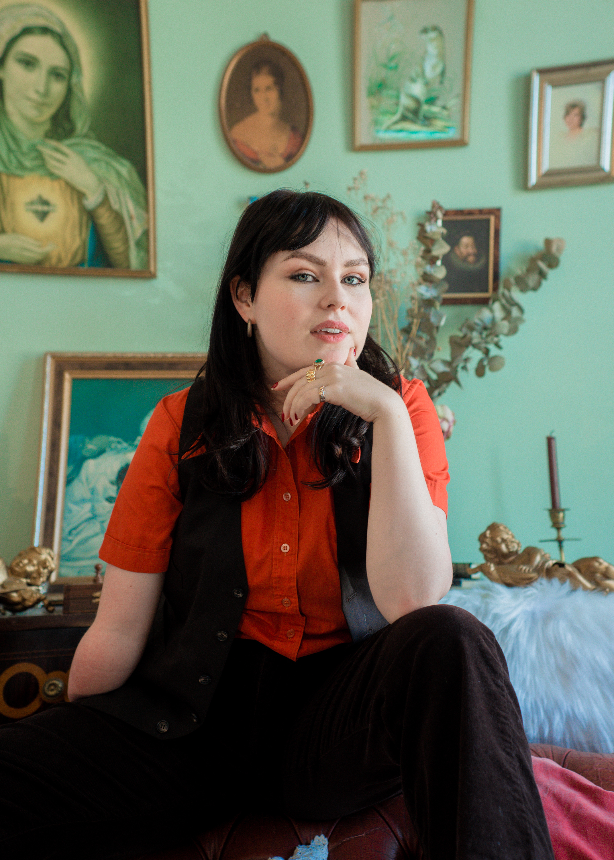Ellie Bleach against a background of portraits hanging on a wall, photographed by Brennan Bucannan