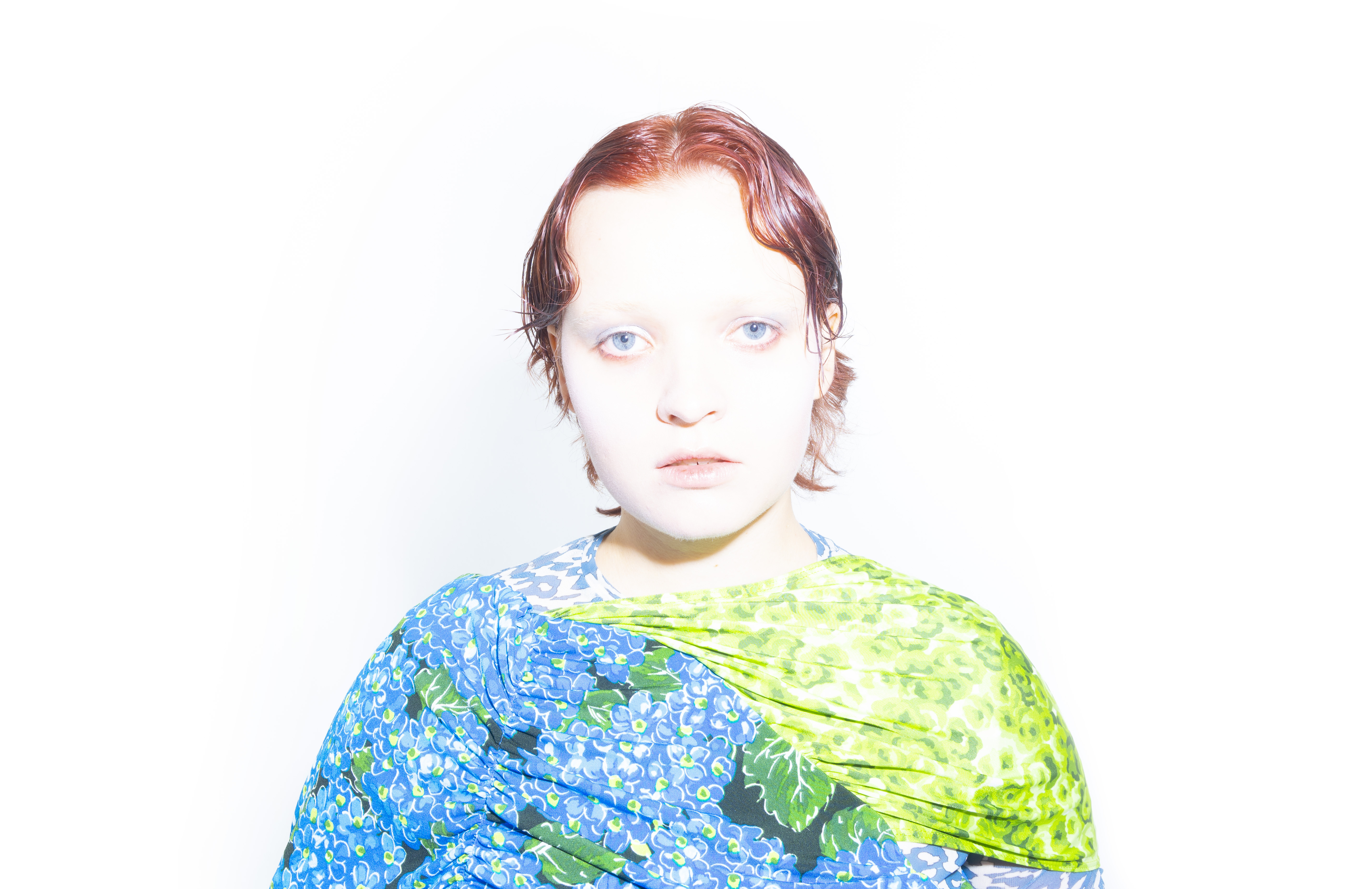 Margrete with red hair and blue-green dress against a plain white background