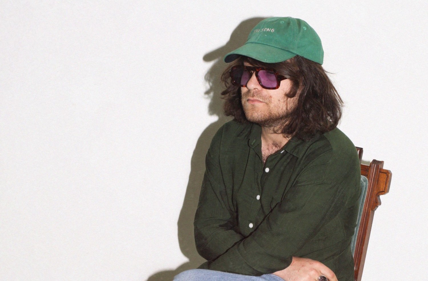 Alex Izenberg wearing sunglasses, green hat and shirt while sitting on chair