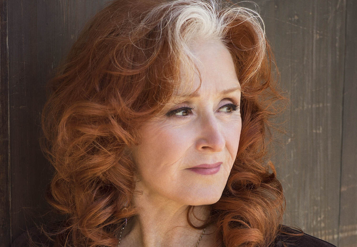 Bonnie Raitt looking off camera wood backdrop