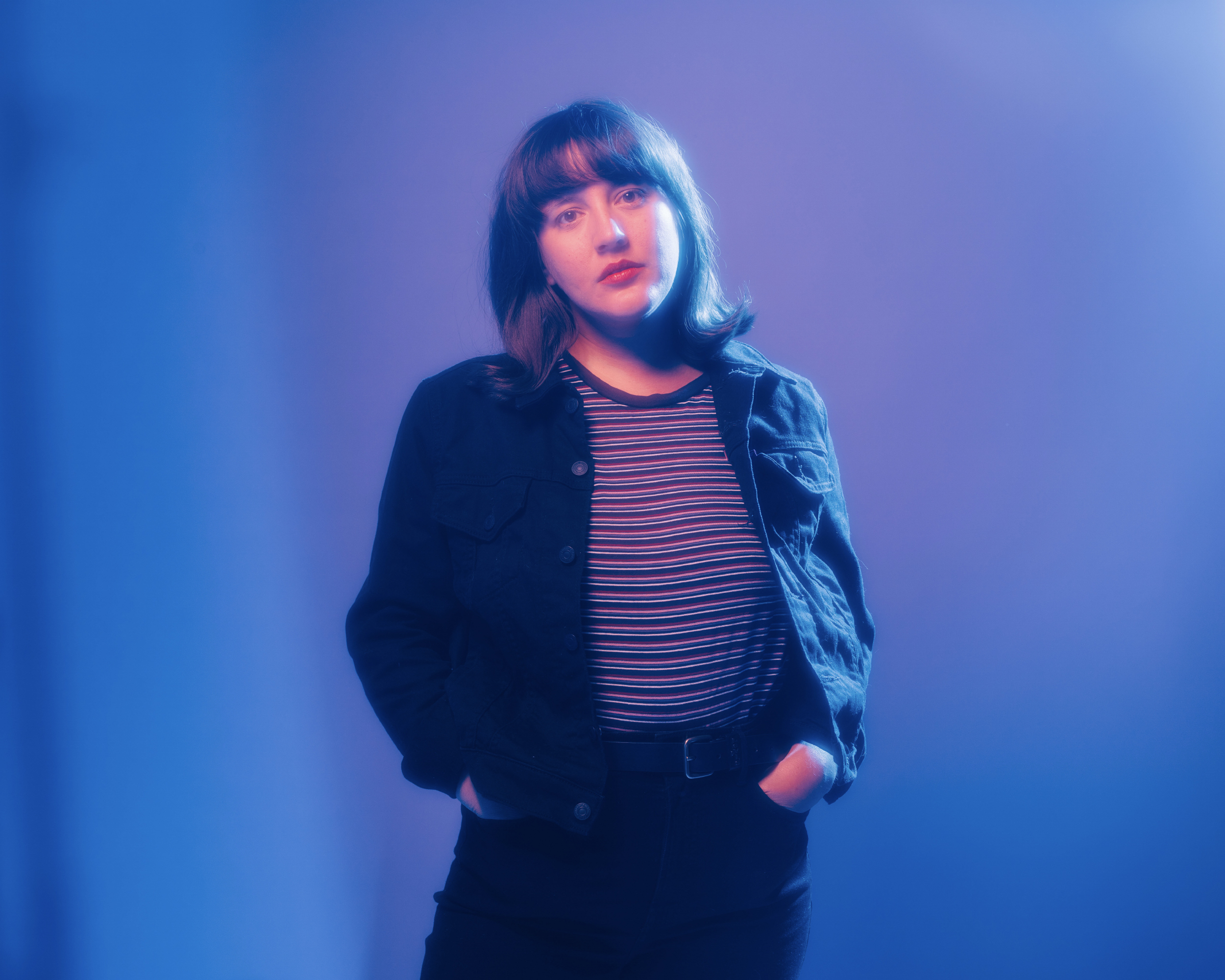 Caitlin Rose with hands in pockets in blue and purple lighting
