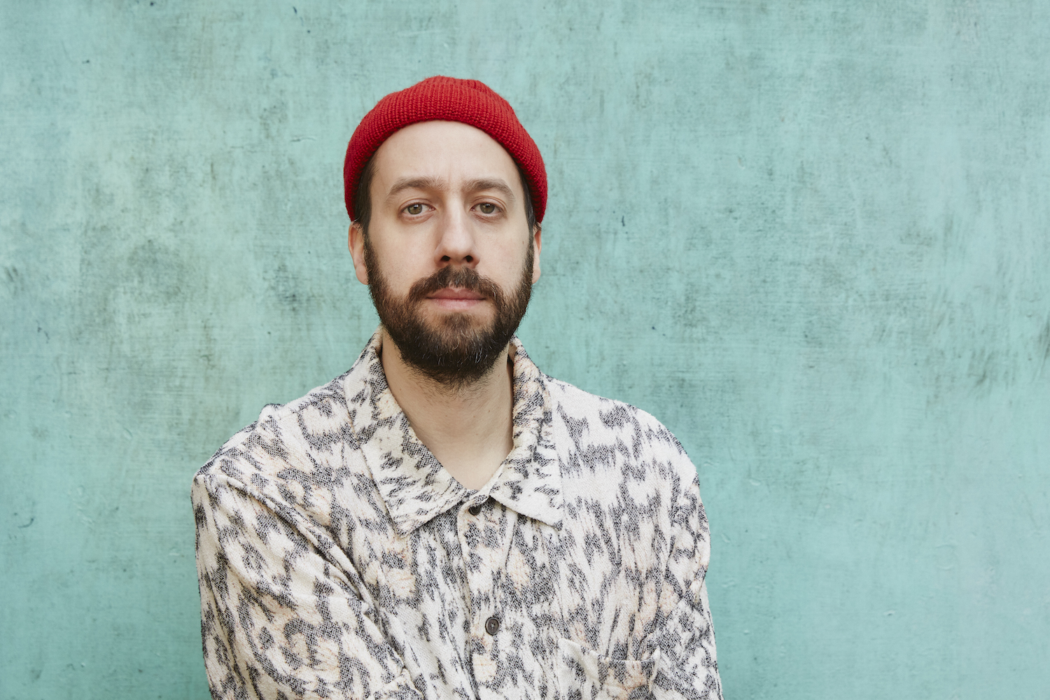 Gold Panda against a blue-green backdrop wearing a red beanie