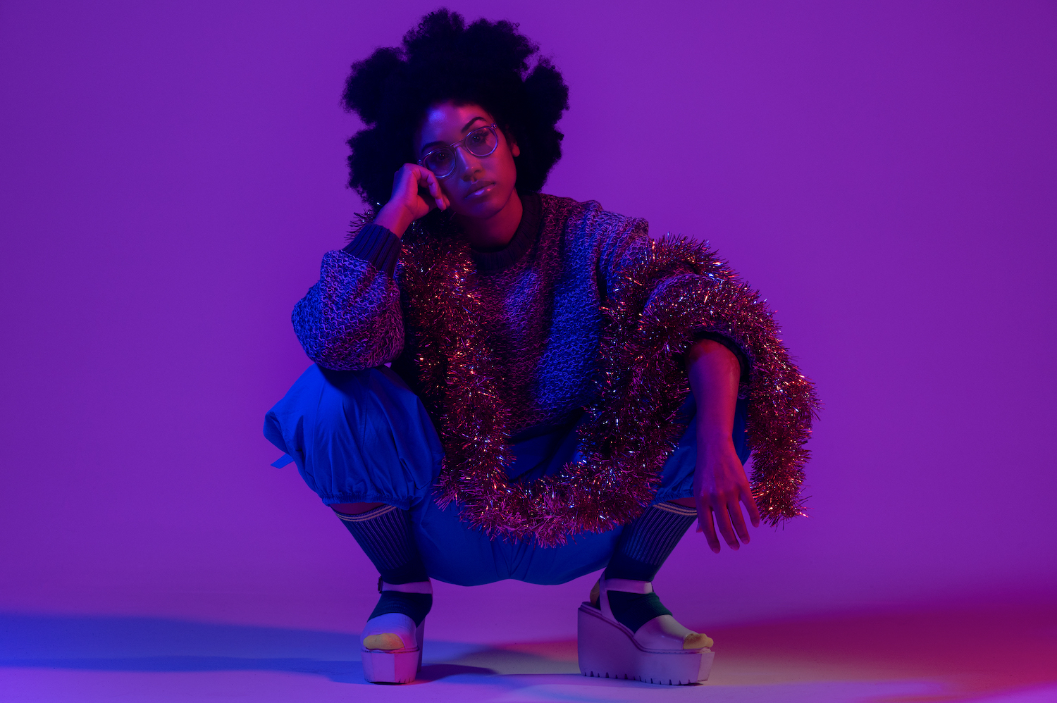 Kadhja Bonet purple lighting crouching with tinsel over arms