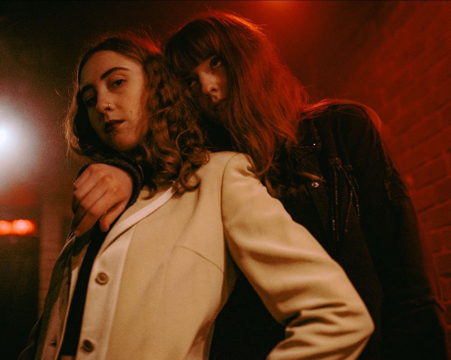Let's Eat Grandma in front of brick wall red lighting