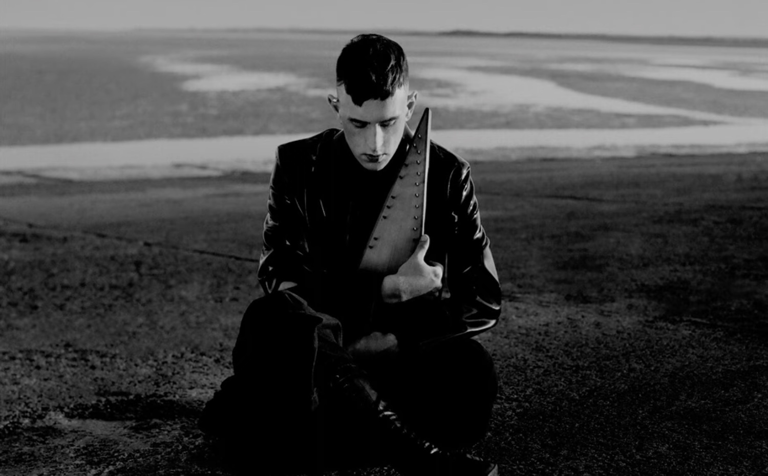 Patrick Wolf sat cross-legged near beach monochrome
