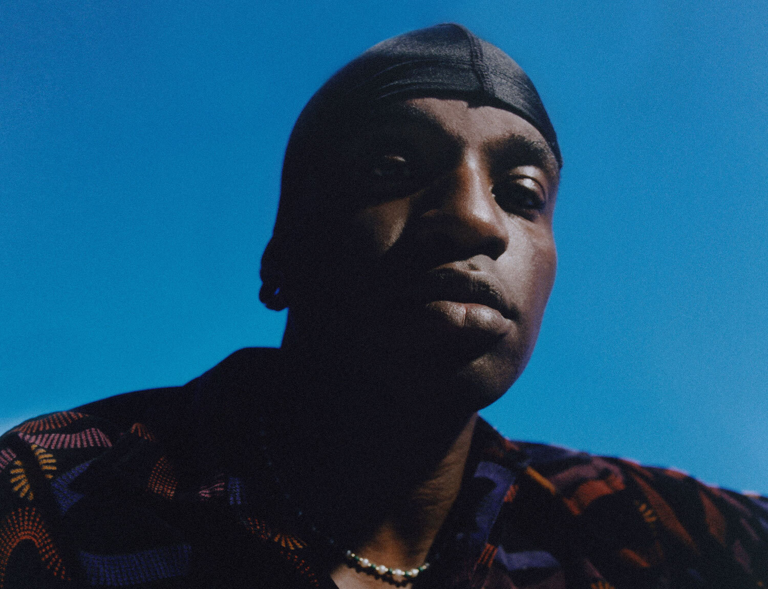 Petite Noir close up looking down a camera blue sky