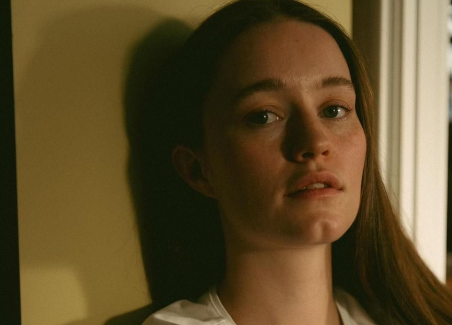 Sigrid leaning against brown wall white t-shirt