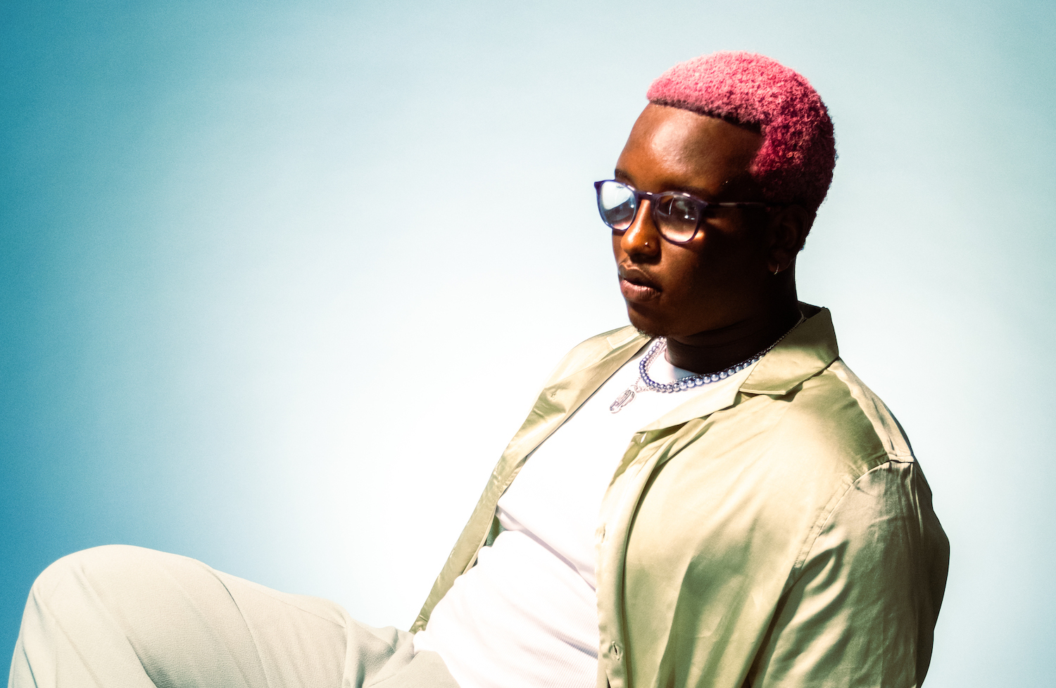 Sipho pink hair blue backdrop sitting on chair