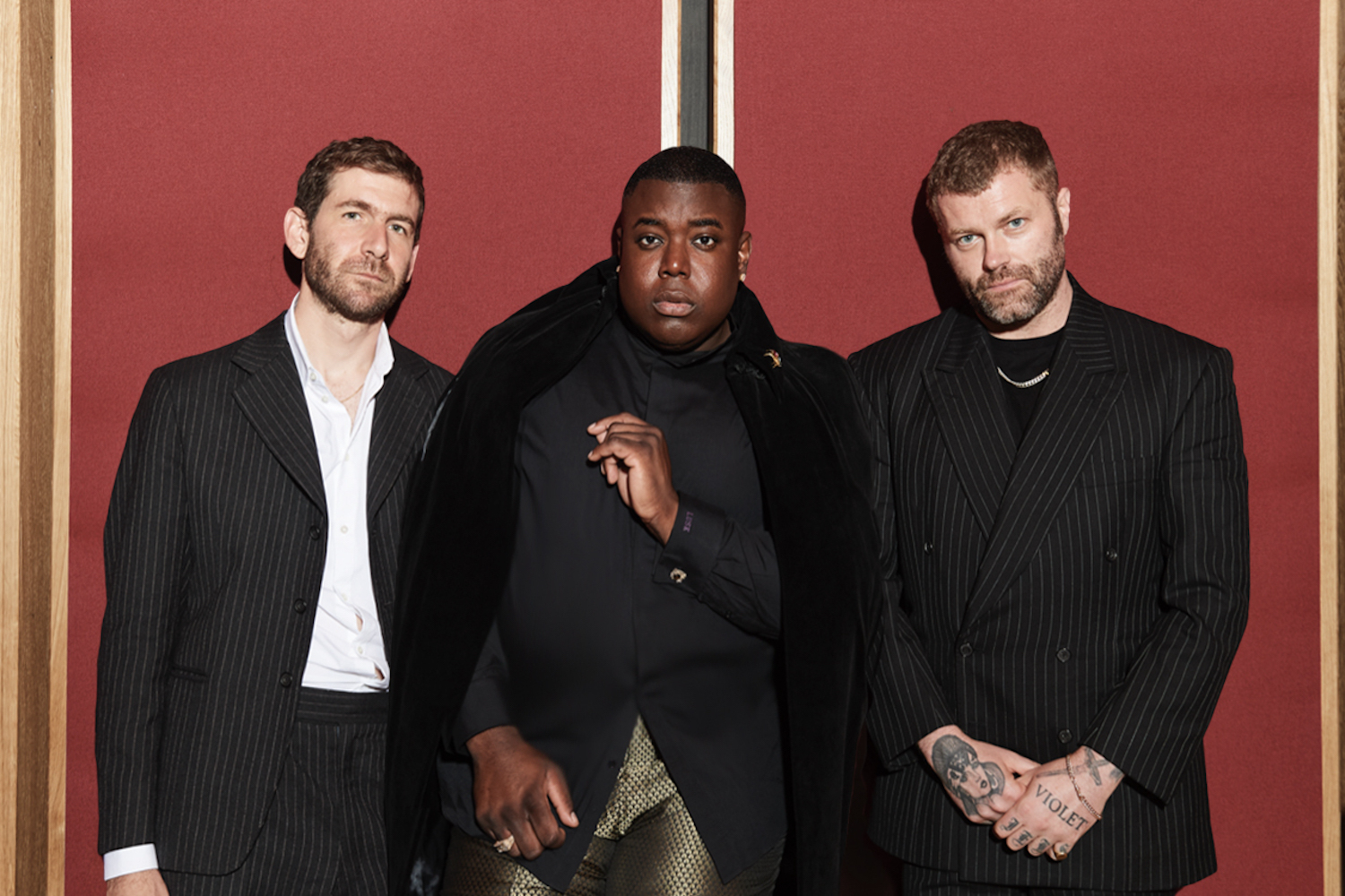 Gabriels stood in front of a red wall in suits