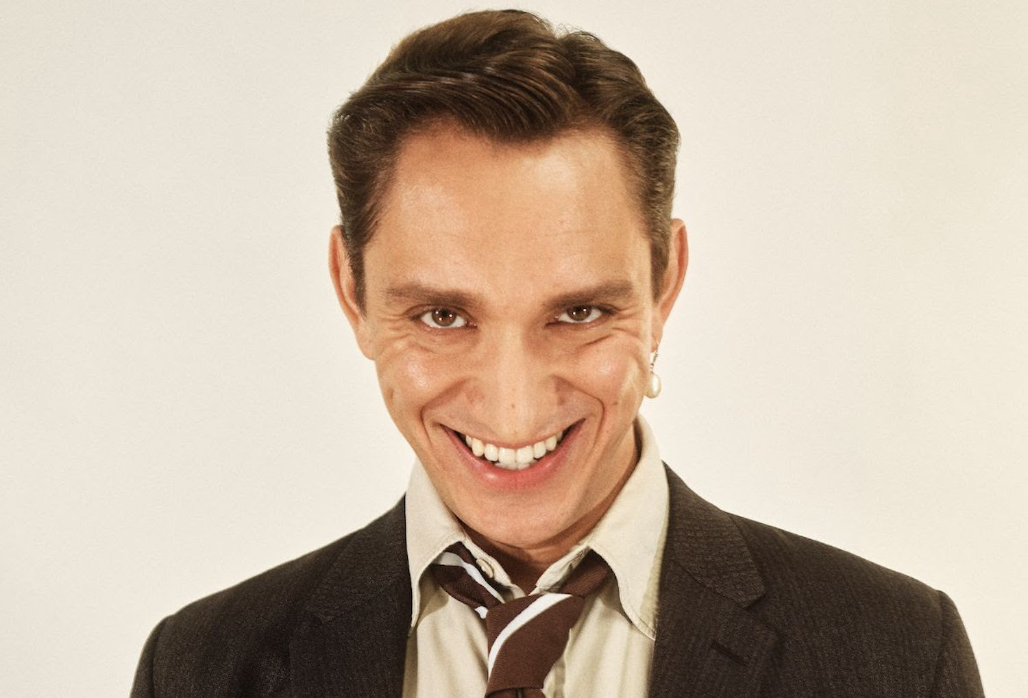 Oliver Sim smiling in a suit for "Run The Credits" single