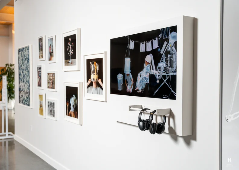Gallery wall of white frames and a large dark artwork depicting children with appliance-like headgear, three black headphones hanging below.