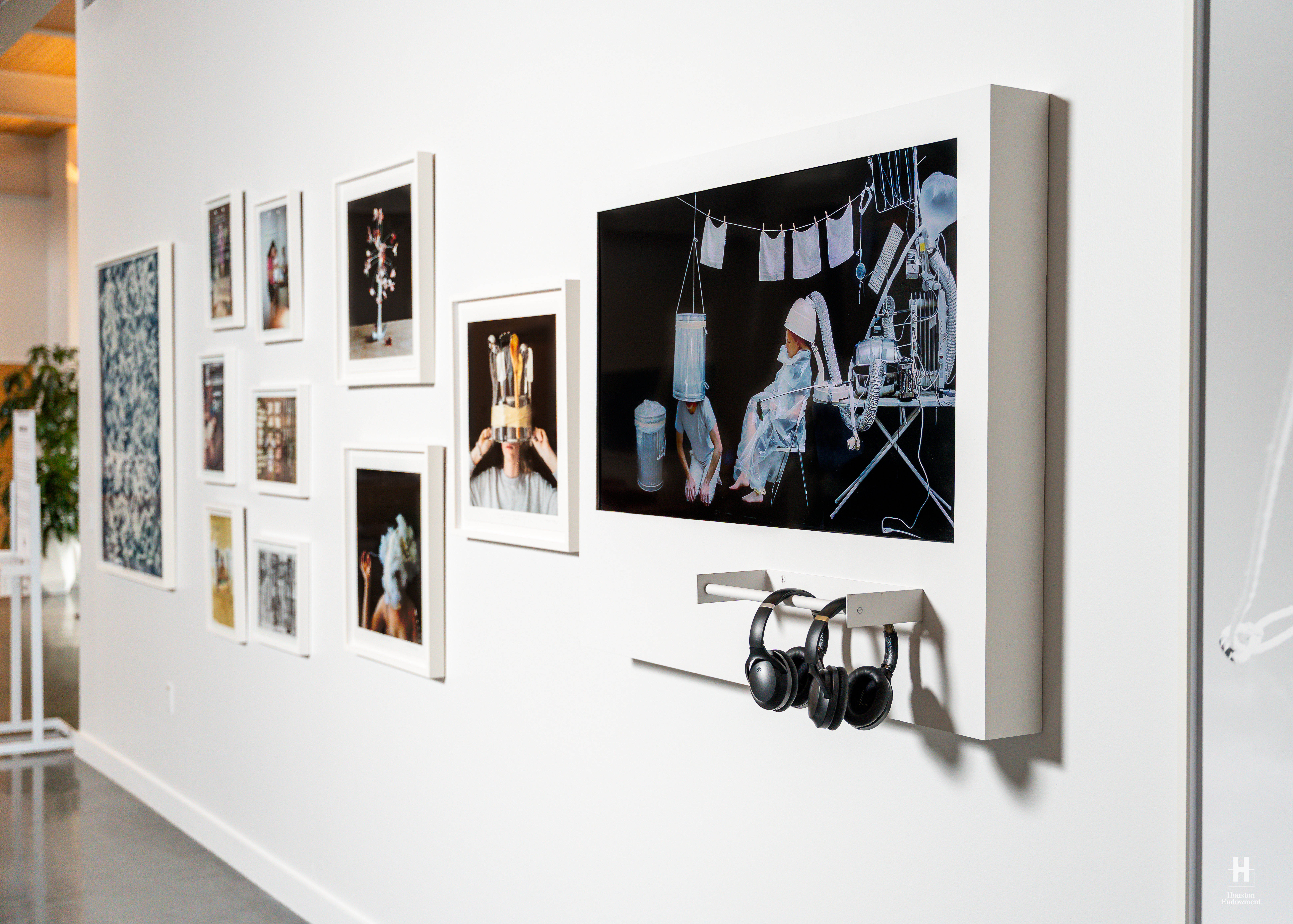 Gallery wall of white frames and a large dark artwork depicting children with appliance-like headgear, three black headphones hanging below.