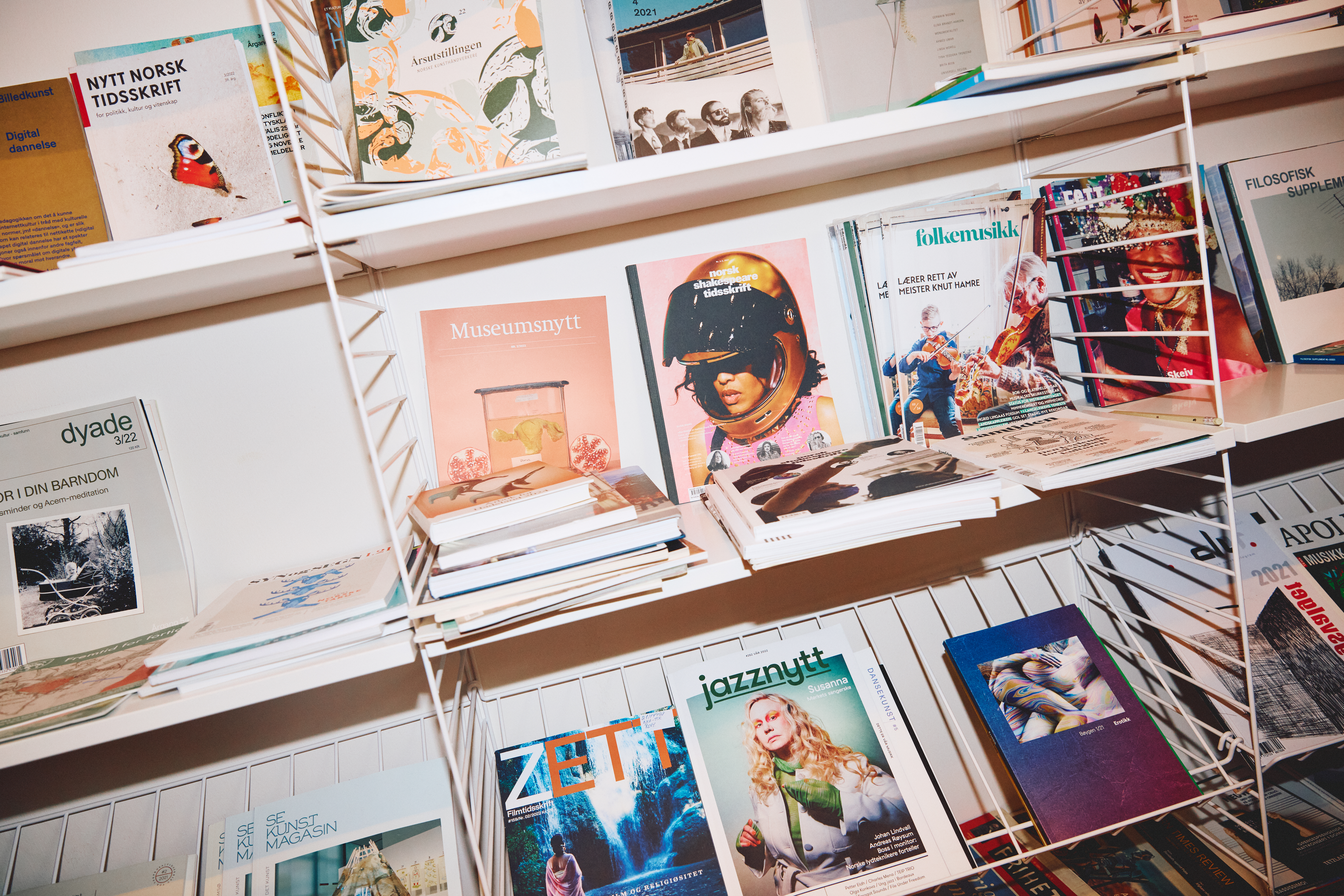 En hylle med ulike magasiner og tidsskrifter utstilt i et stativ, med fargerike forsider som viser kunst, musikk og kultur.