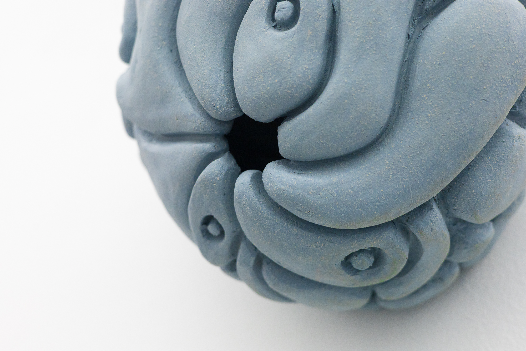 Nært bilde av en keramisk skulptur som forestiller en detaljert og abstrakt hjerne, malt i en jevn, lyseblå farge.