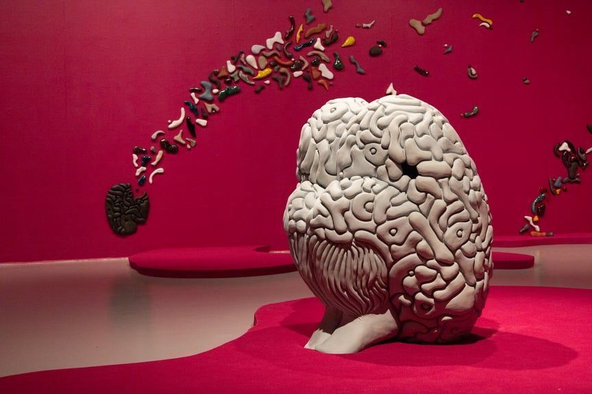 Skulptur av en hvit hjerne i et rødt rom med fargerike former på veggen.