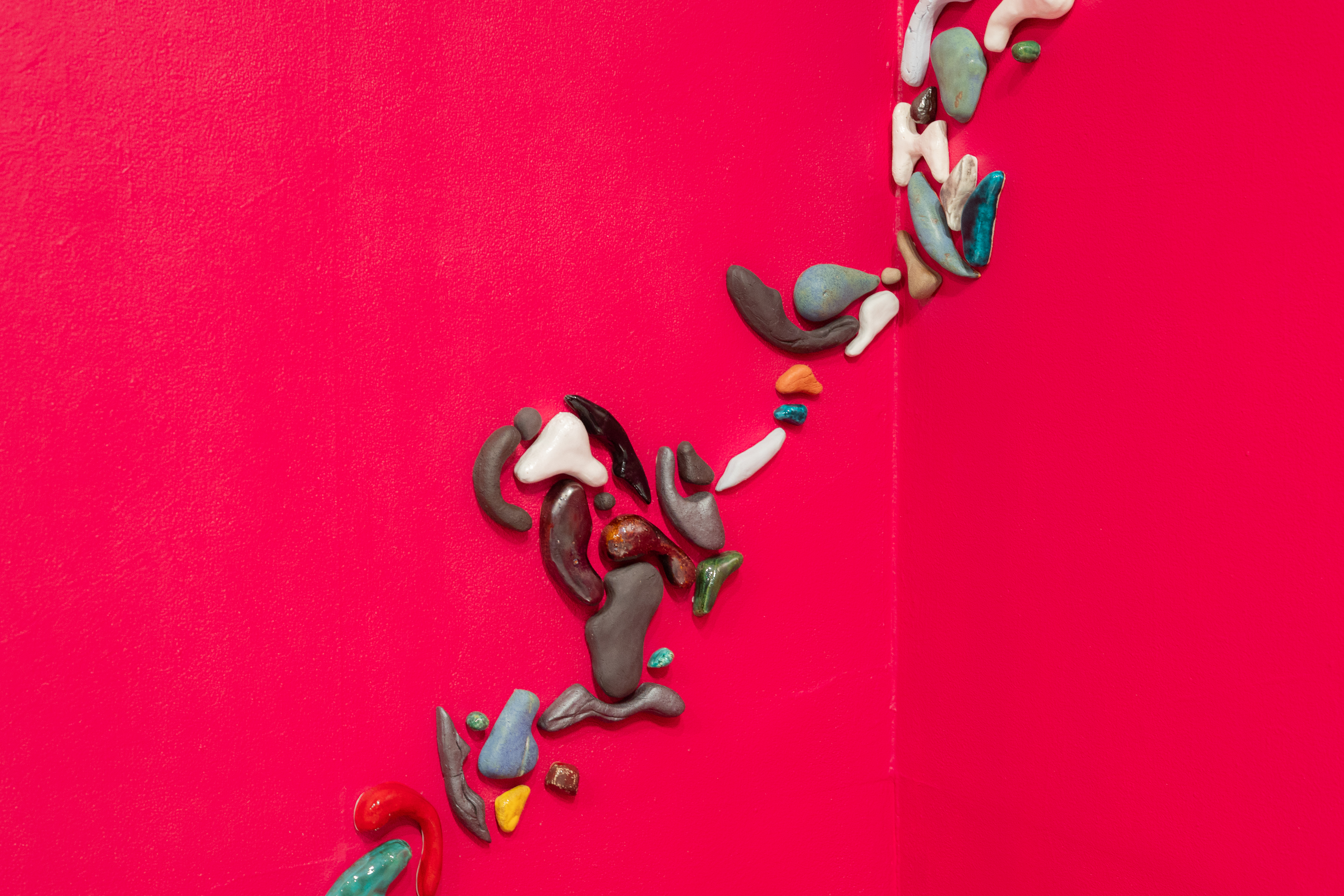 Nærbilde av små, uregelmessige former i ulike farger som er festet til en knallrød vegg, arrangert i en buet linje.