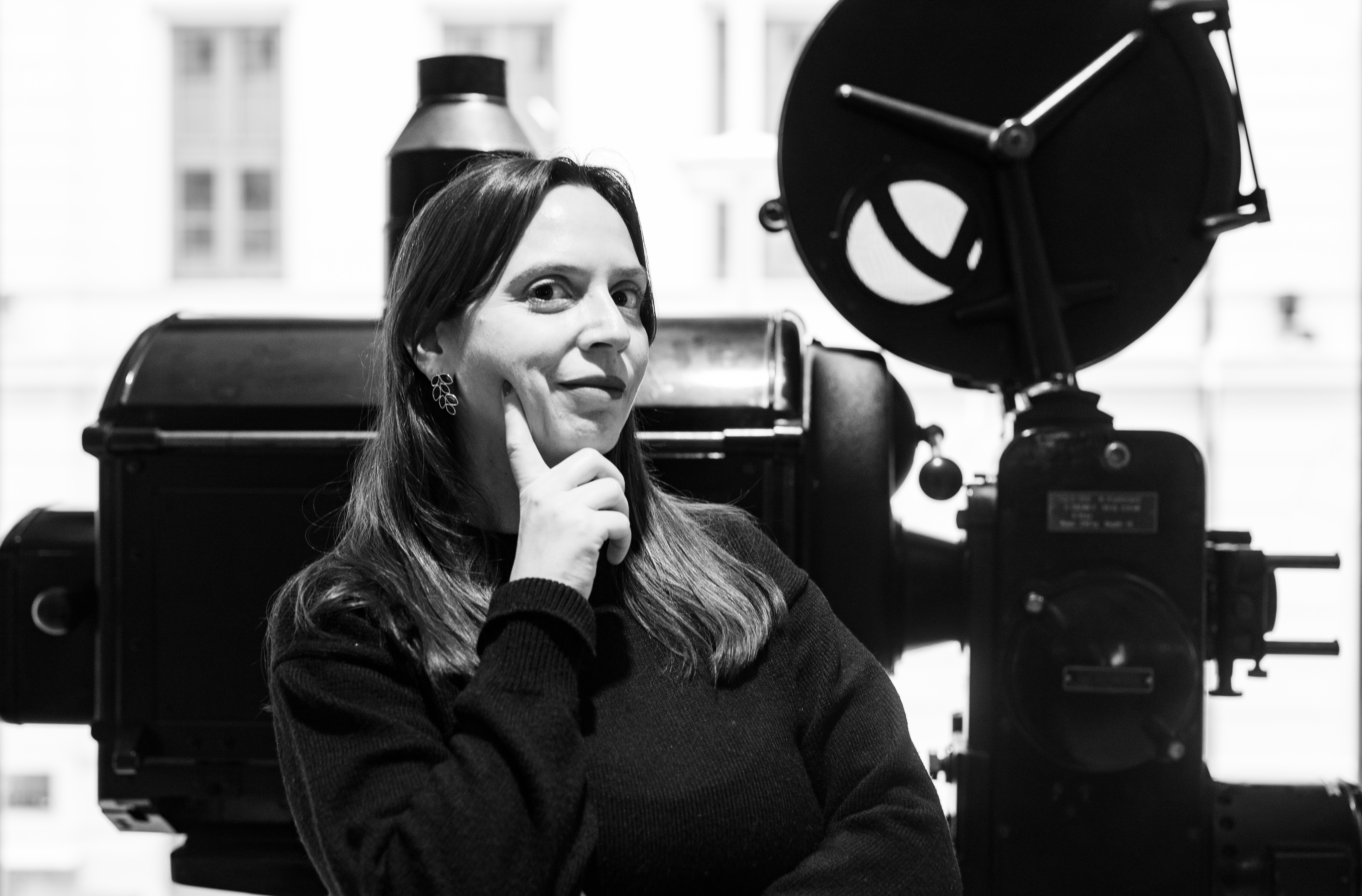 Laura Pedrali står foran en gammel filmfremviser. Bildet er i svart hvitt.