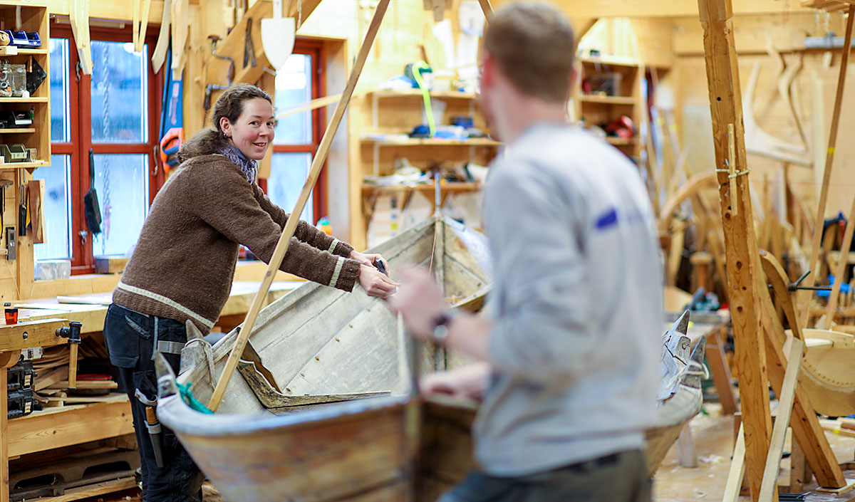 Bildet viser to personer som jobber med å bygge en tradisjonell båt.