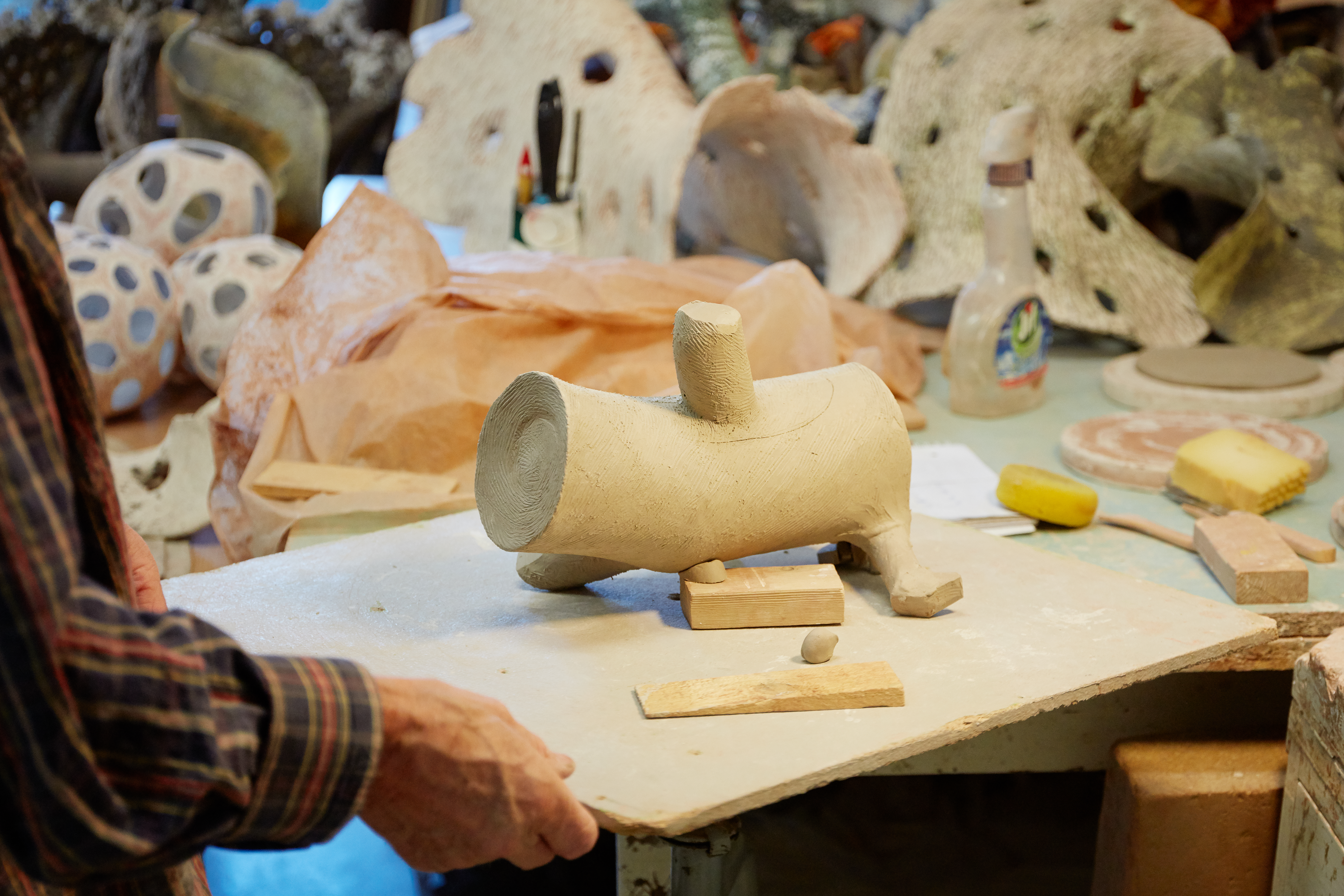 En person som arbeider med en leire- eller gipsskulptur av en dyrefigur i et kunststudio.