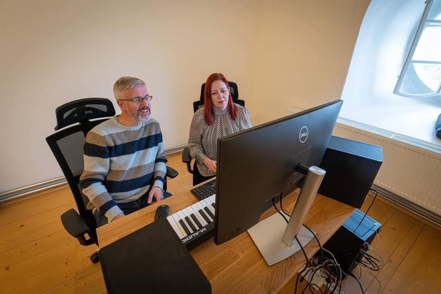 Bildet viser to mennesker som sitter foran en dataskjerm med et keyboard.