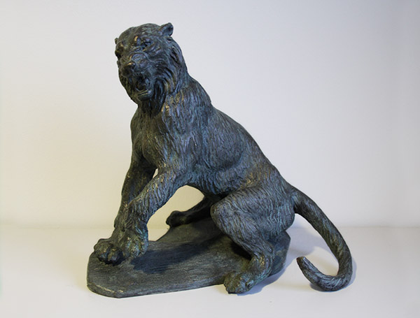 En mørk bronsefarget skulptur av en løve som sitter med halen buet til siden.