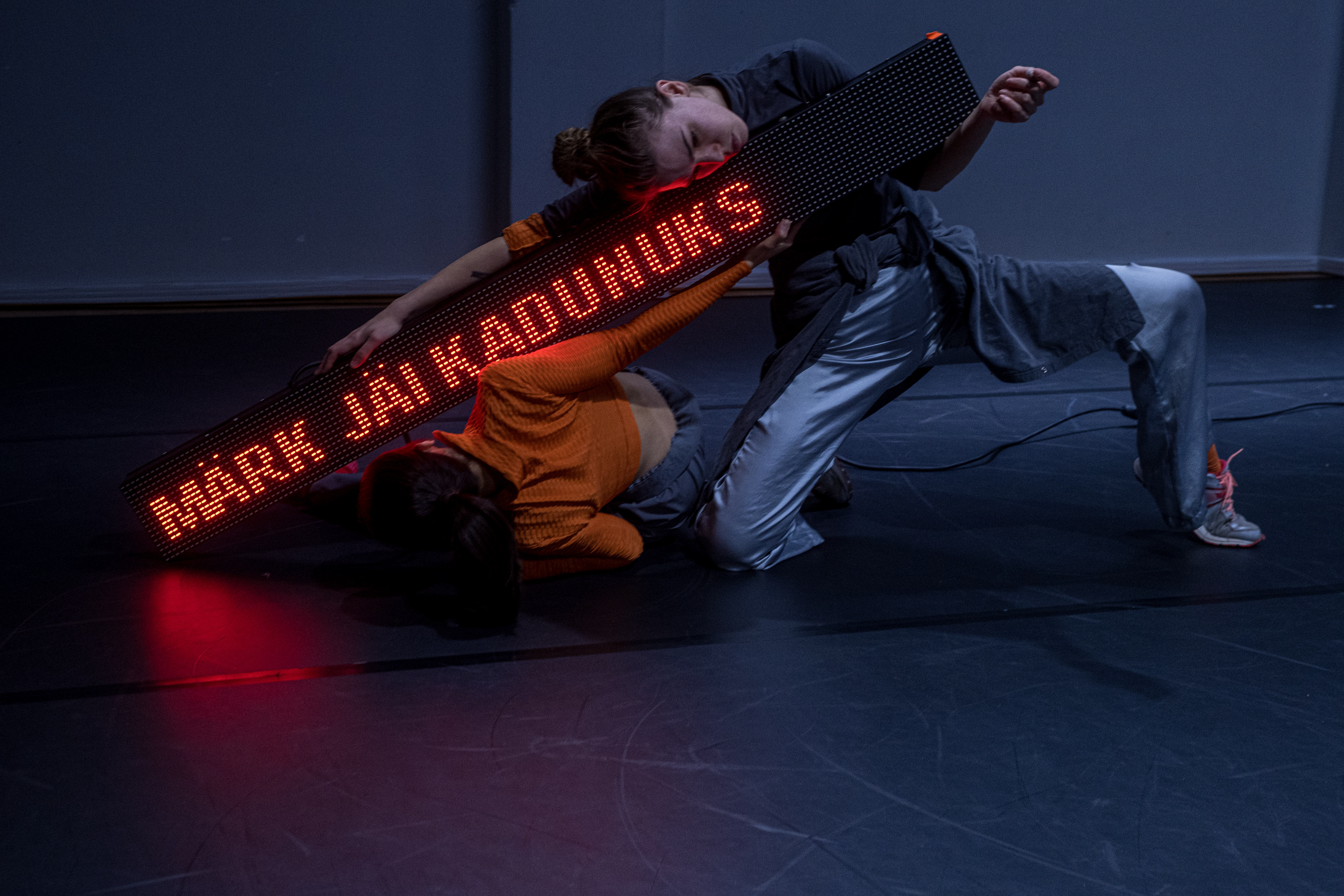 Bildet viser to dansere som holder en digital tekstfremviser med estisk tekst.