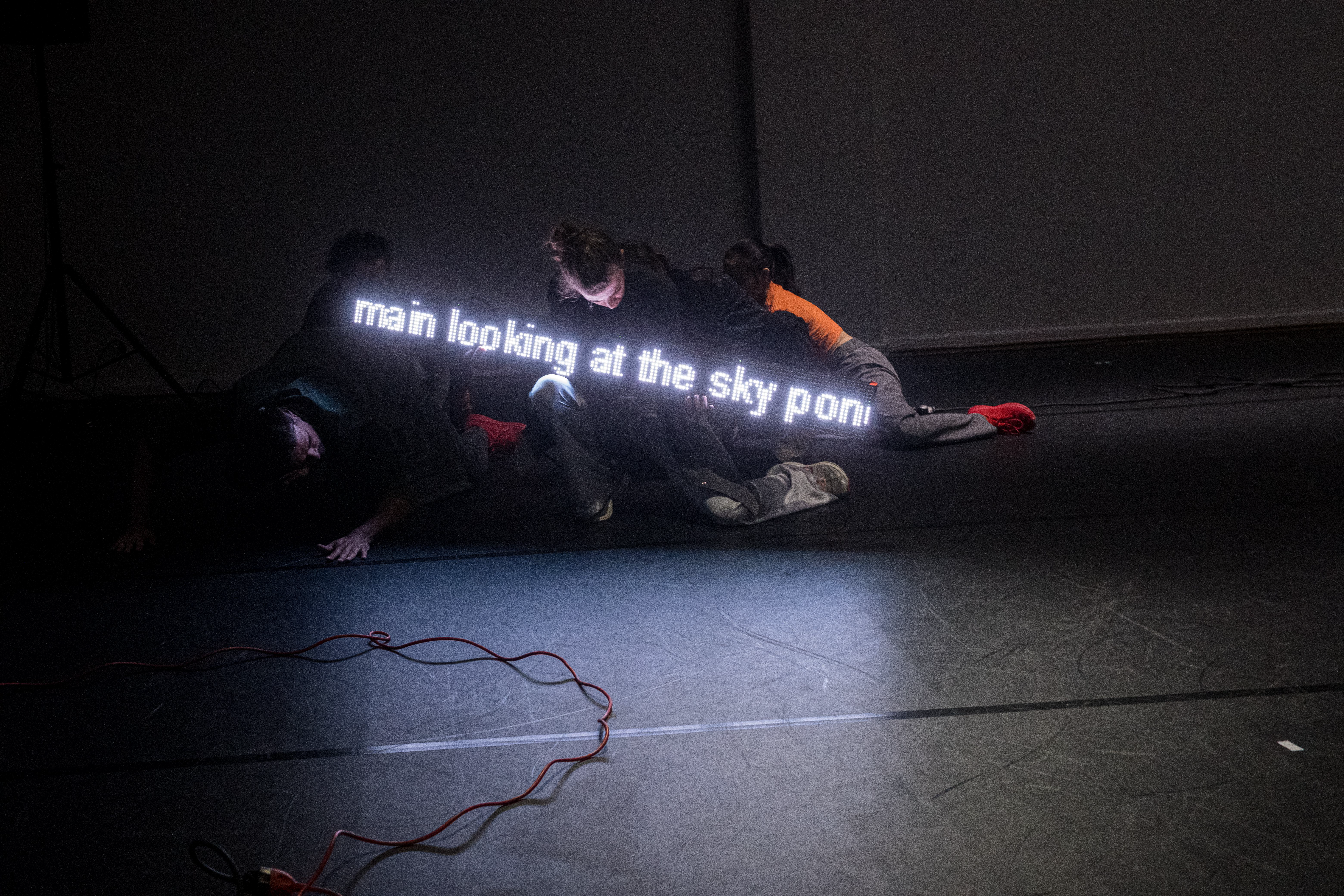 Bildet viser fire dansere som beveger seg på gulvet med en lysende tekstfremviser.