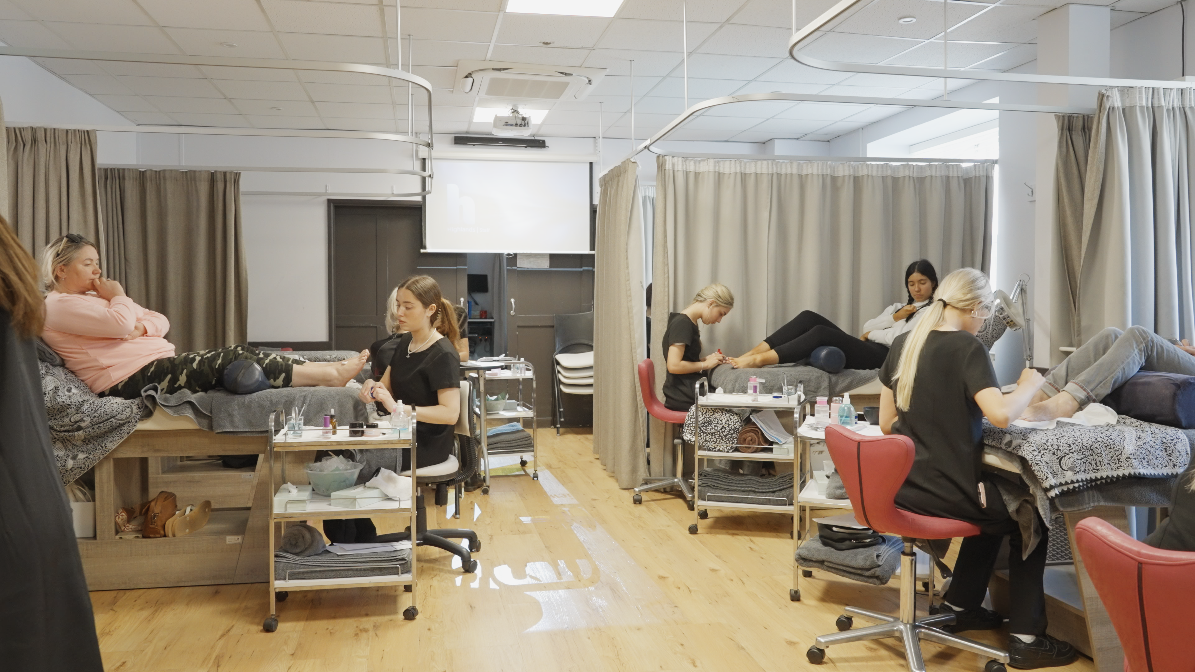 A wide shot of a salon environment filled with people receiving various treatments, from painted toe nails to foot massages.