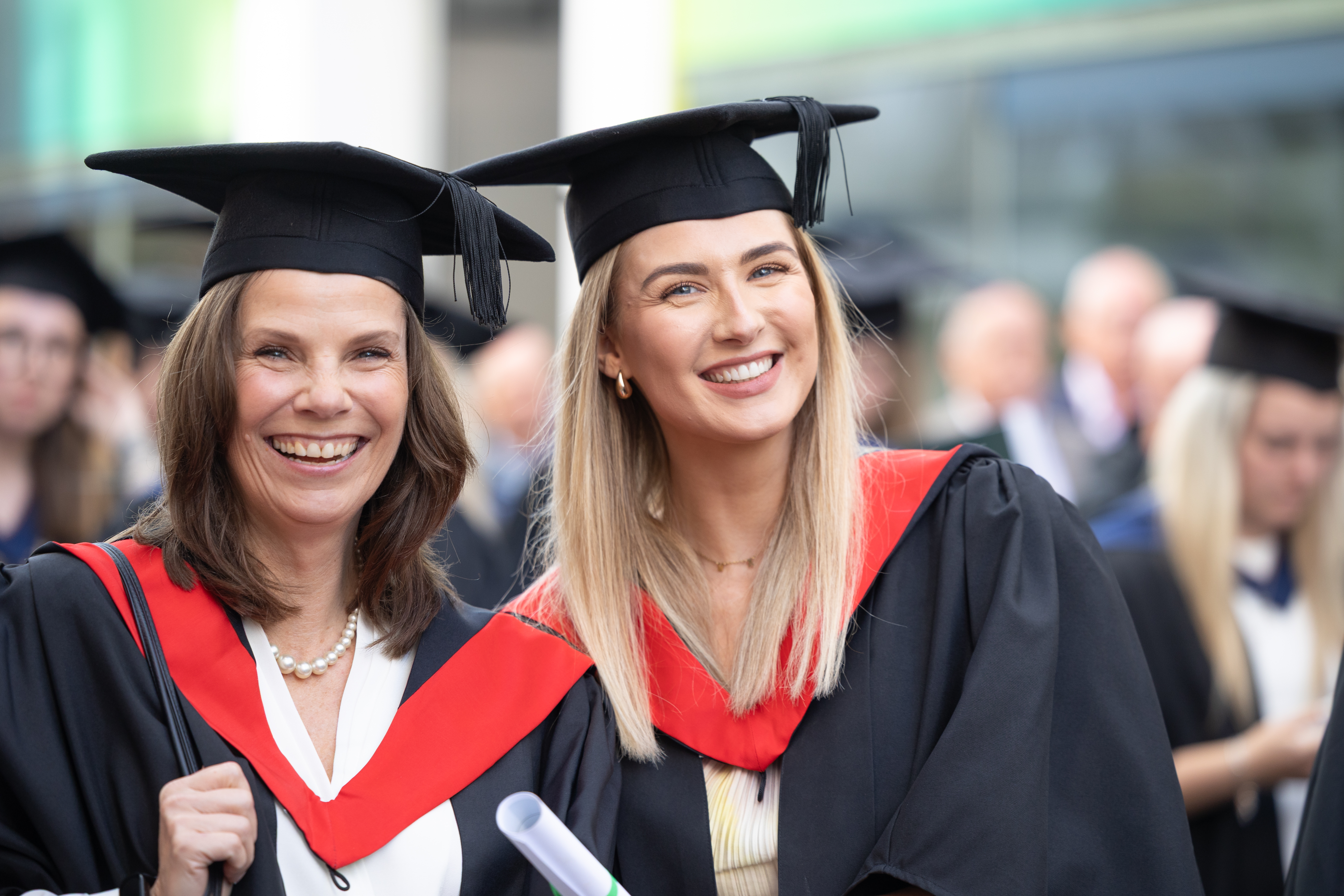 Two University College Jersey graduates smile for a photograph in their academic dress during the graduation celebrations.