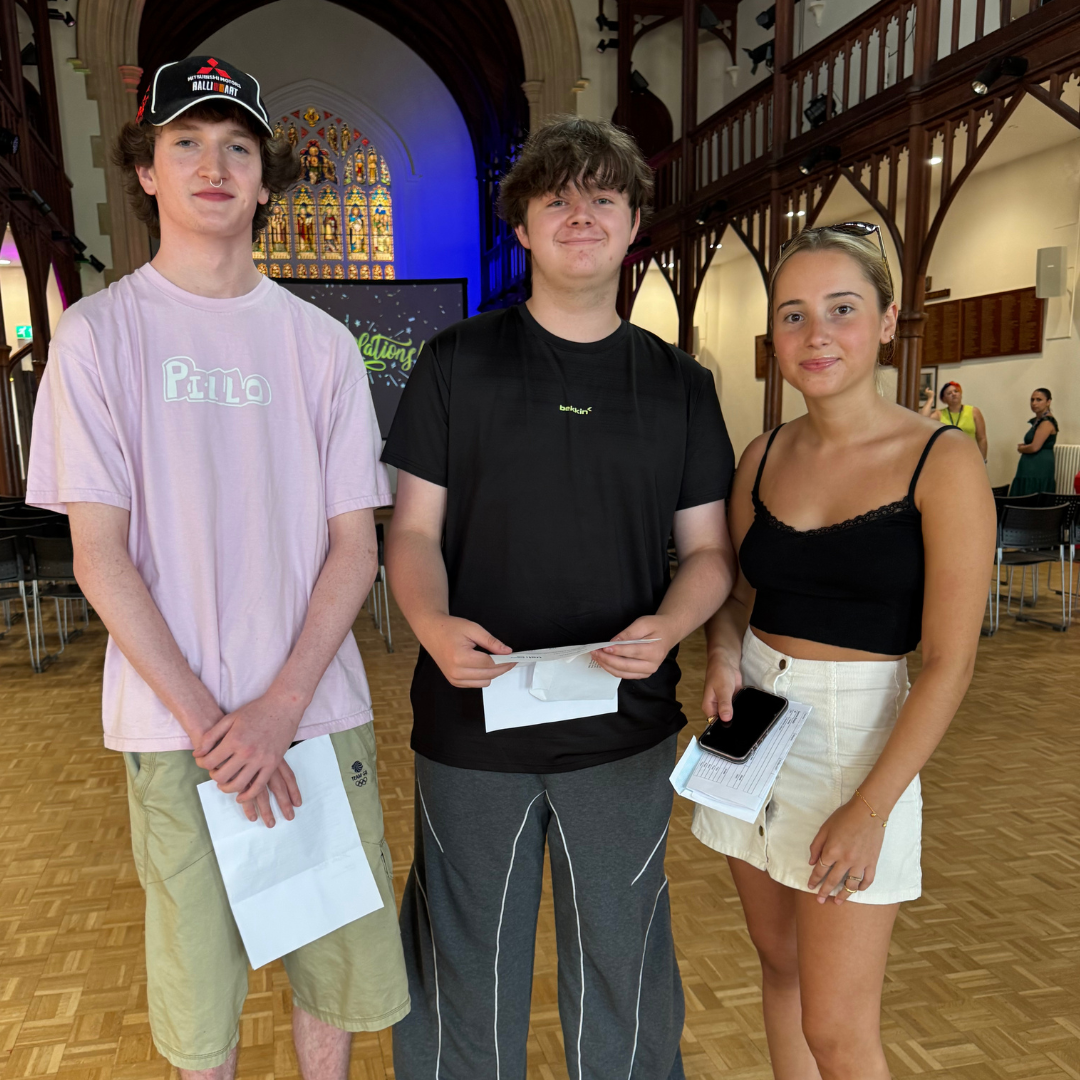 Three students in the great hall smiling while collecting their results.