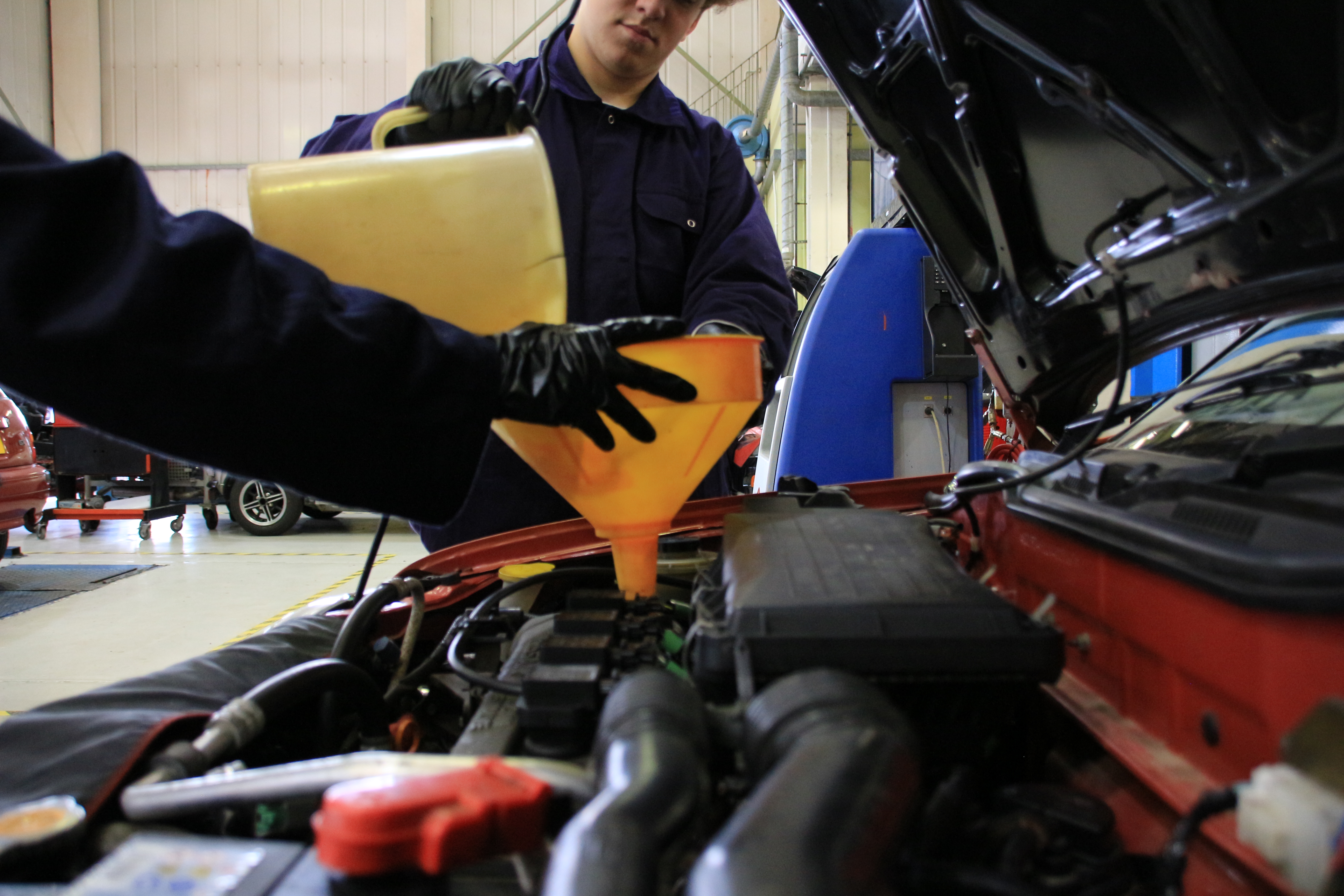6th-Form - Student Filing a Car With Coolant in a Workshop