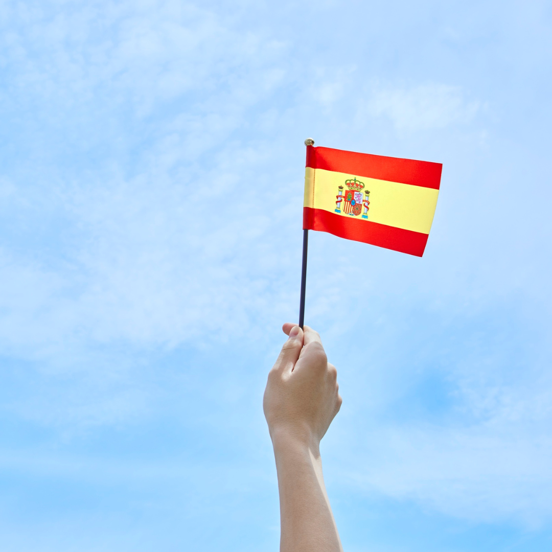 An image of a hand holding a Spanish flag up against a blue sky.