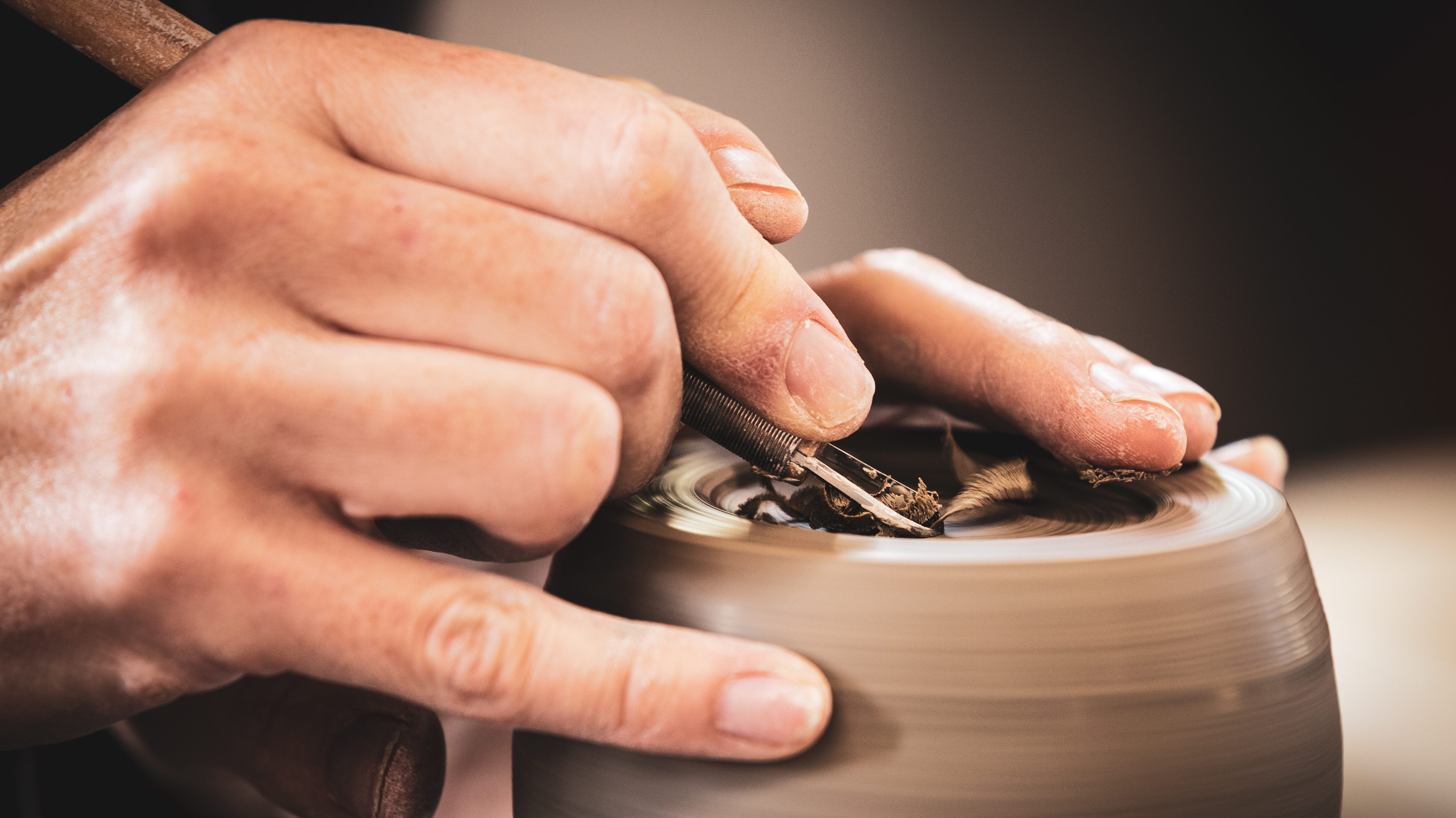 Hands on pottery wheel whilst carving into the top of a pot.