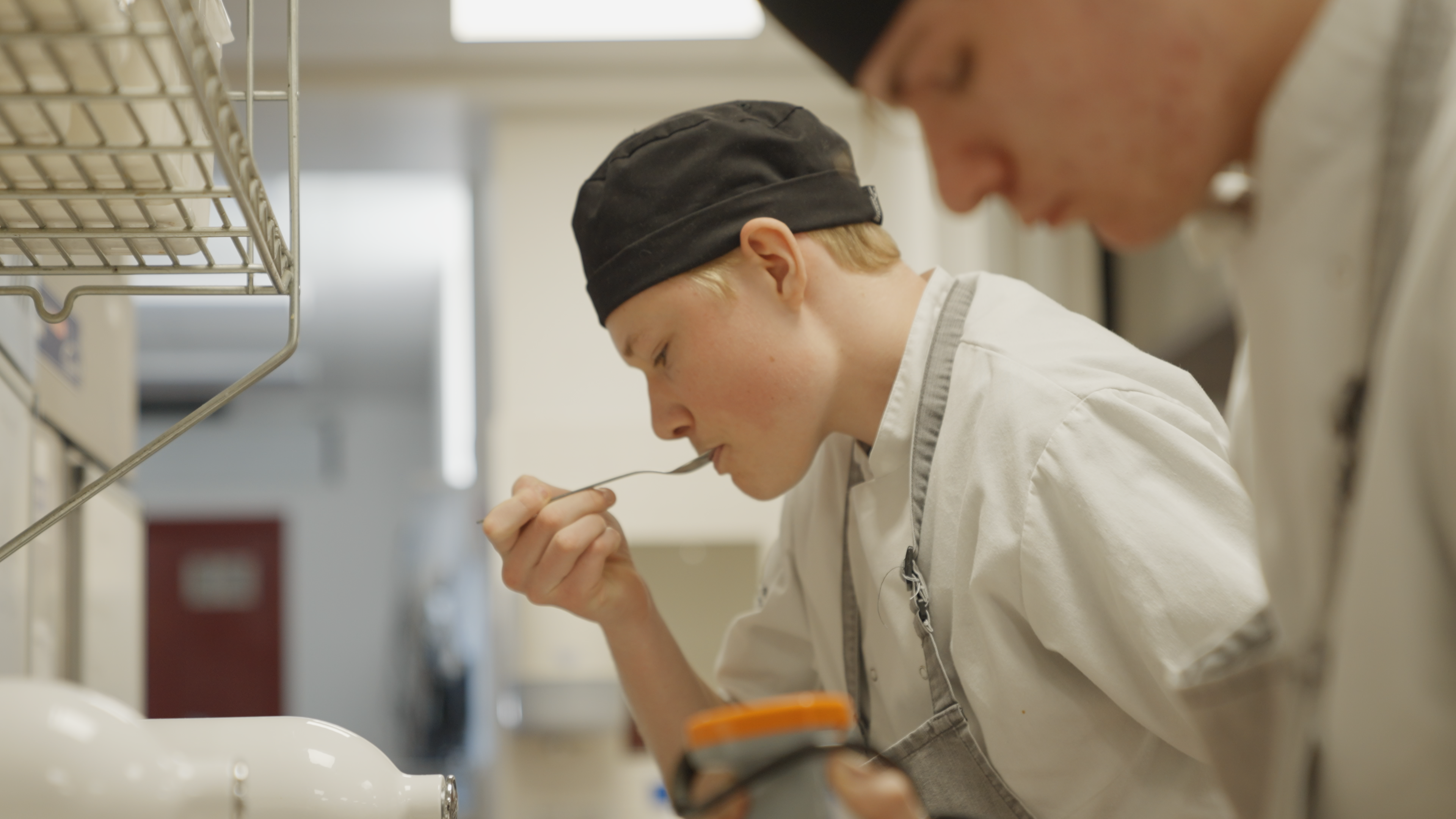 A medium close up of a kitchen setting with a chef tasting their food from a spoon.
