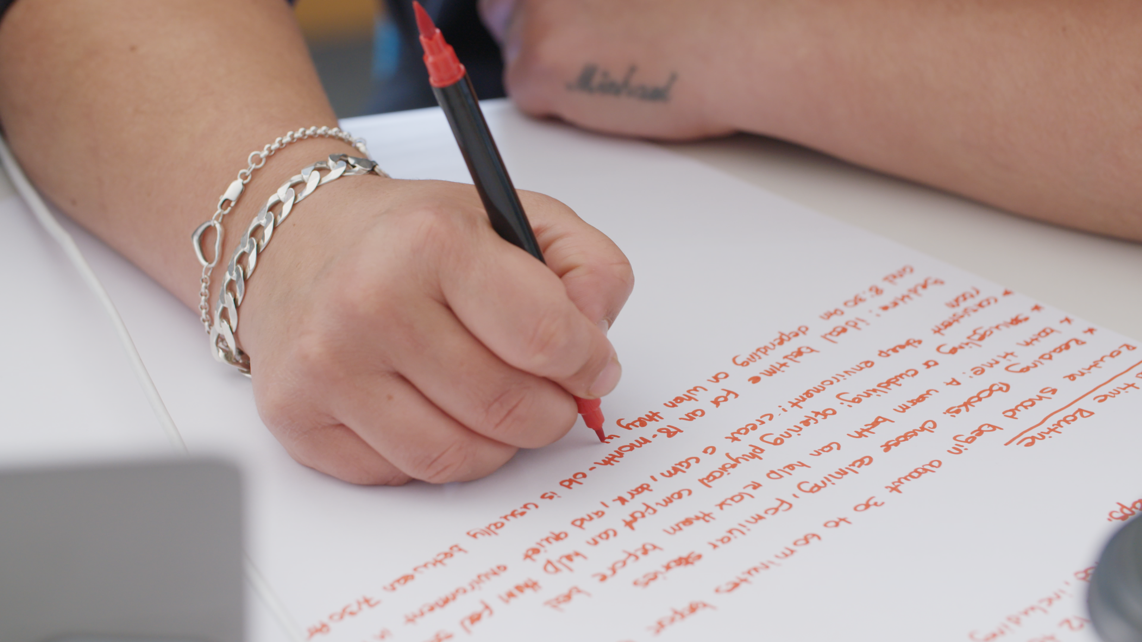 A close up of a hand using a red pen to write notes on a sheet of blank paper.