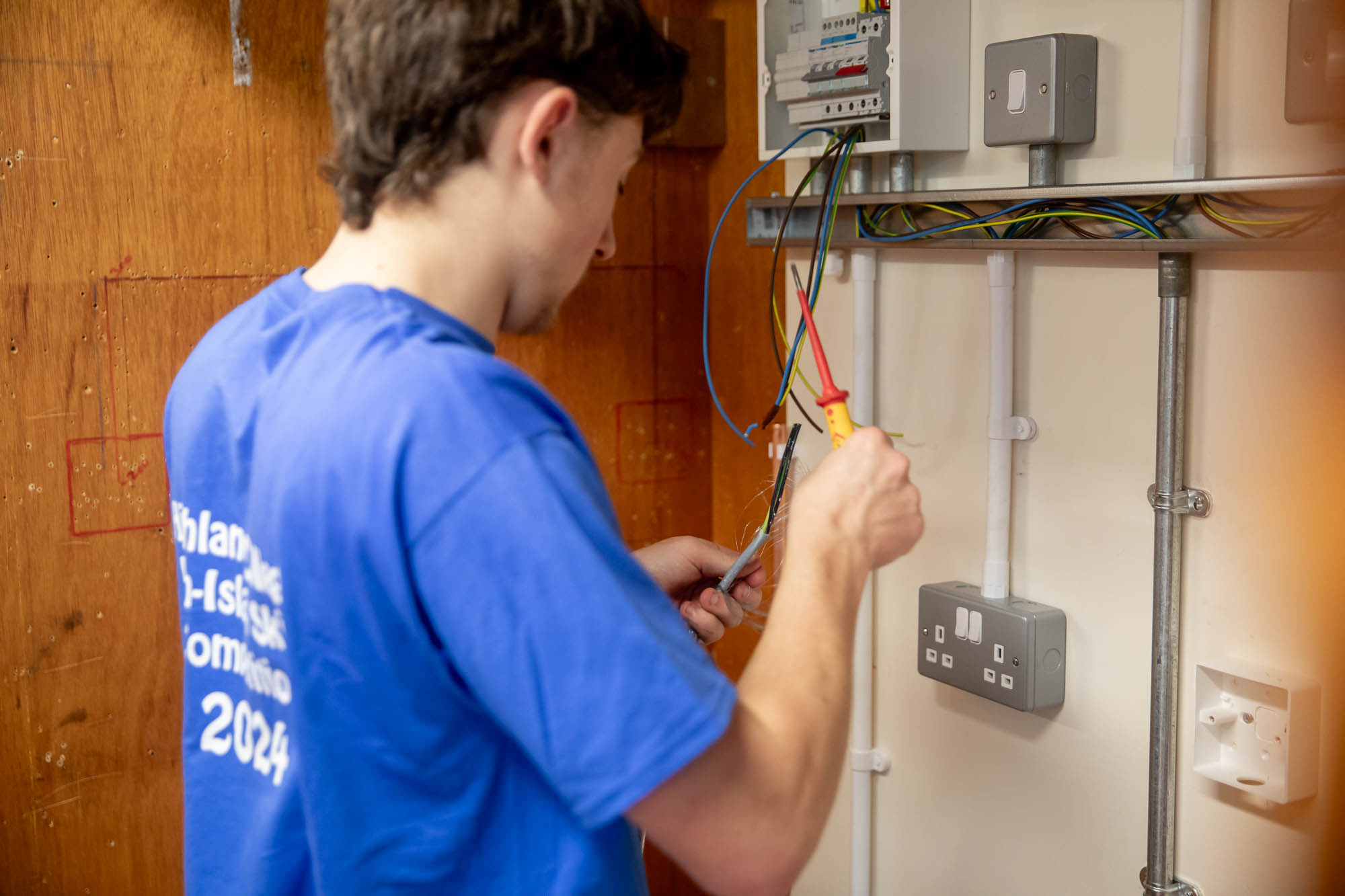 A medium close up of a person working on an electrical panel, handling wires and tools with sockets and switches visible.