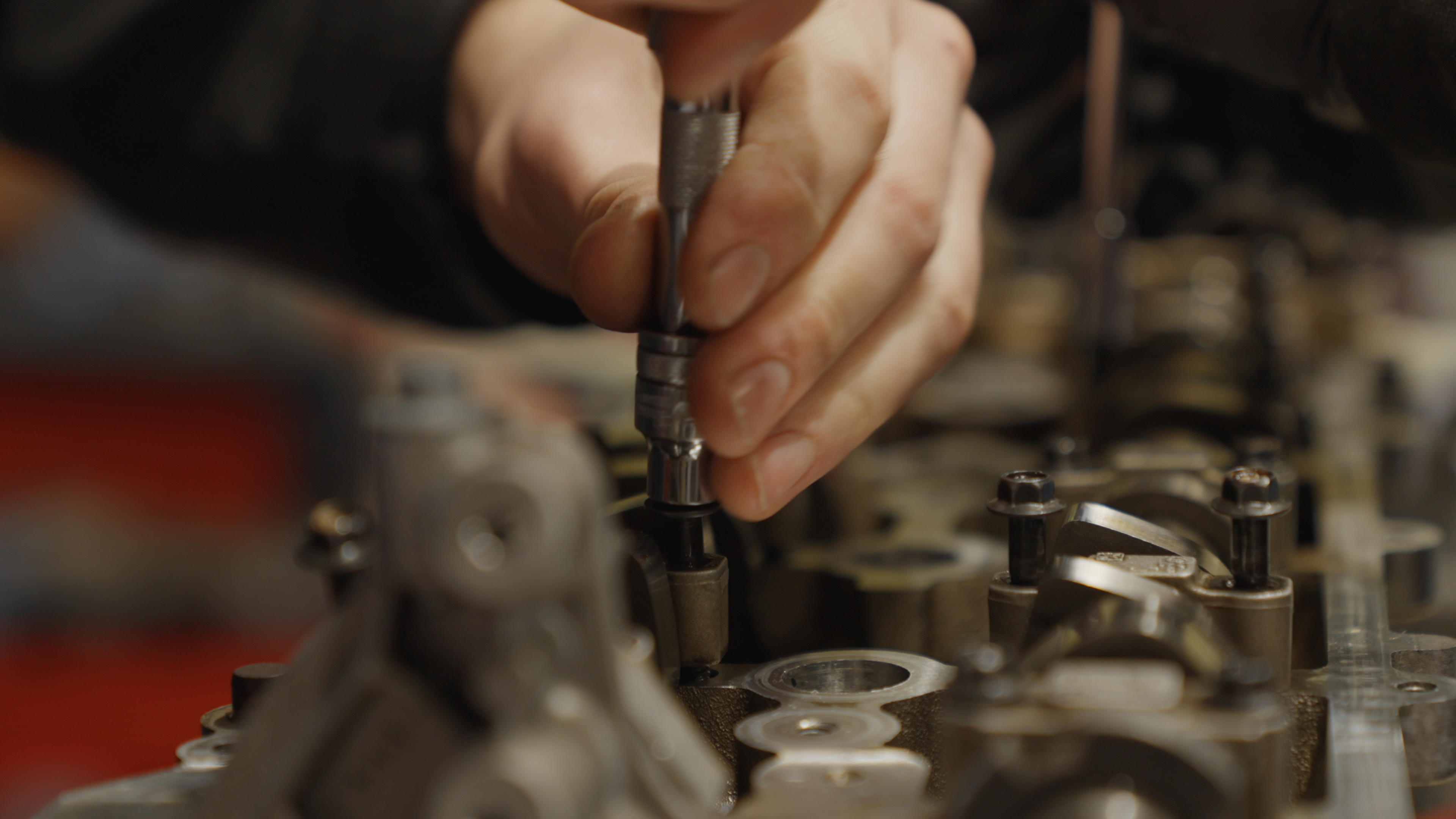 A close up shot of a hand using a small socket wrench to work on a car engine.