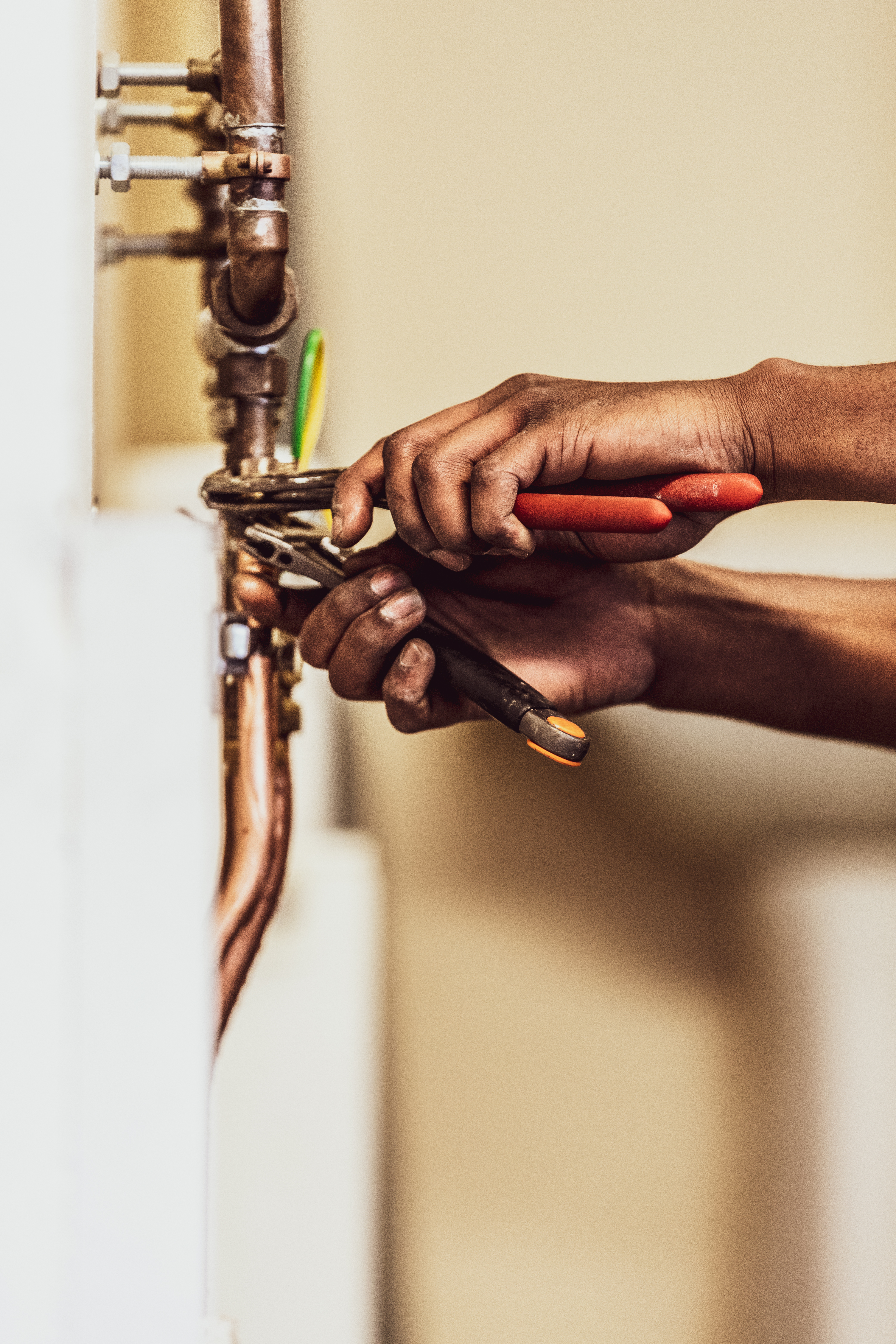 Closeup of hands using pliers to adjust copper pipes, focusing on the tools and pipework with a blurred background.