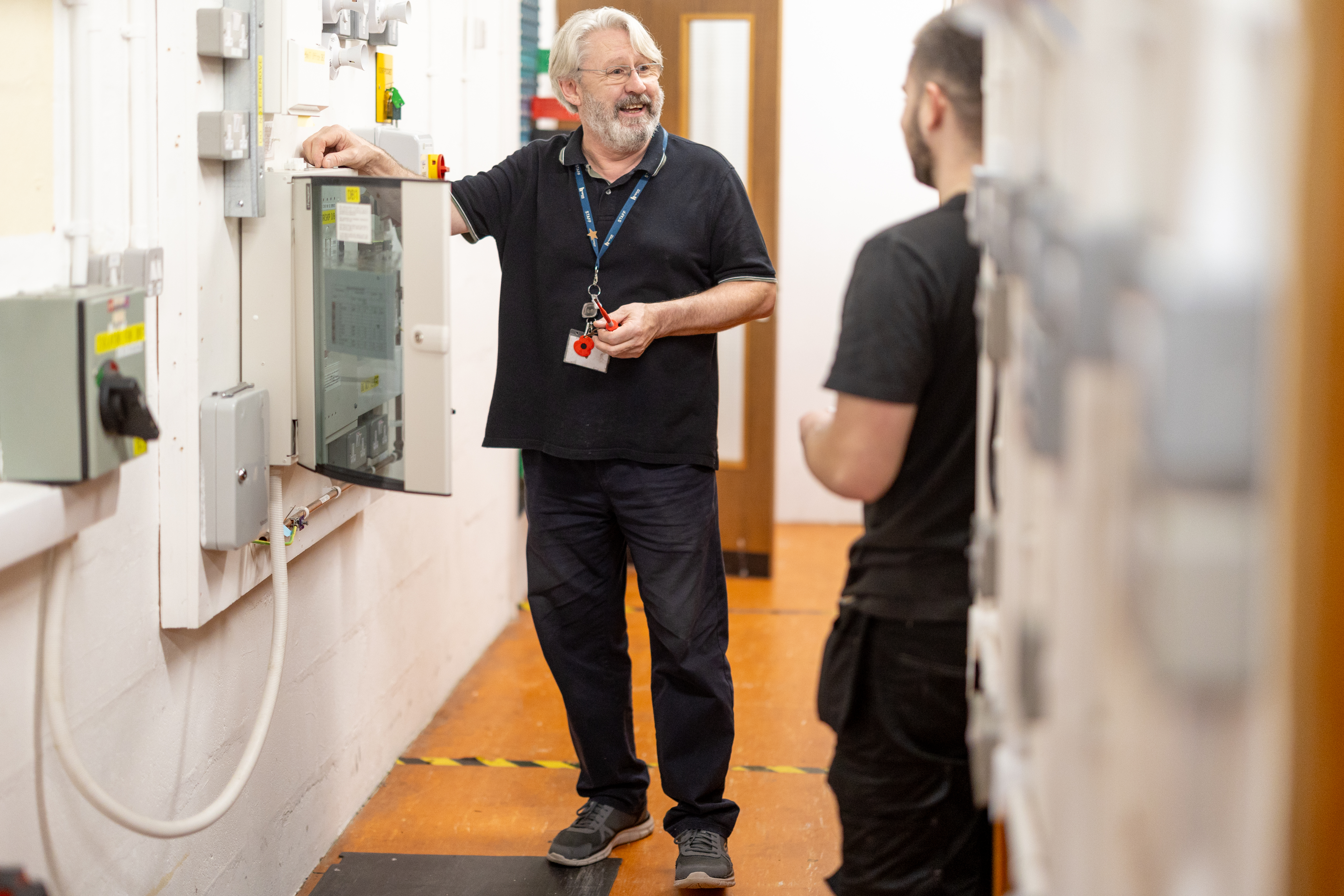 Students at Highlands College examining an open electrical panel in a hallway with mounted equipment and caution tape on the floor.
