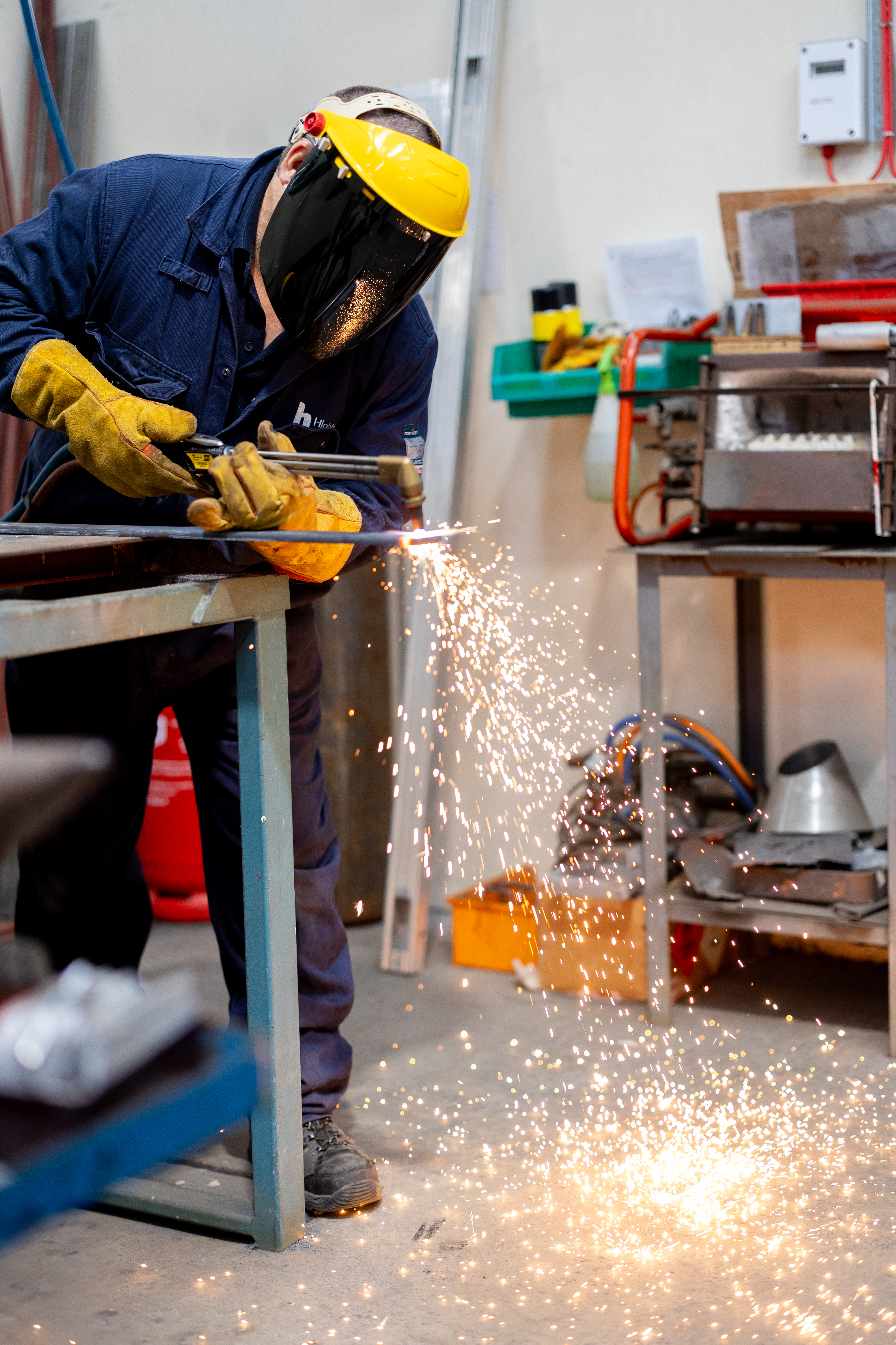 Engineering student at Highlands College using a power tool to cut metal in a workshop, with sparks flying and safety gear in use.