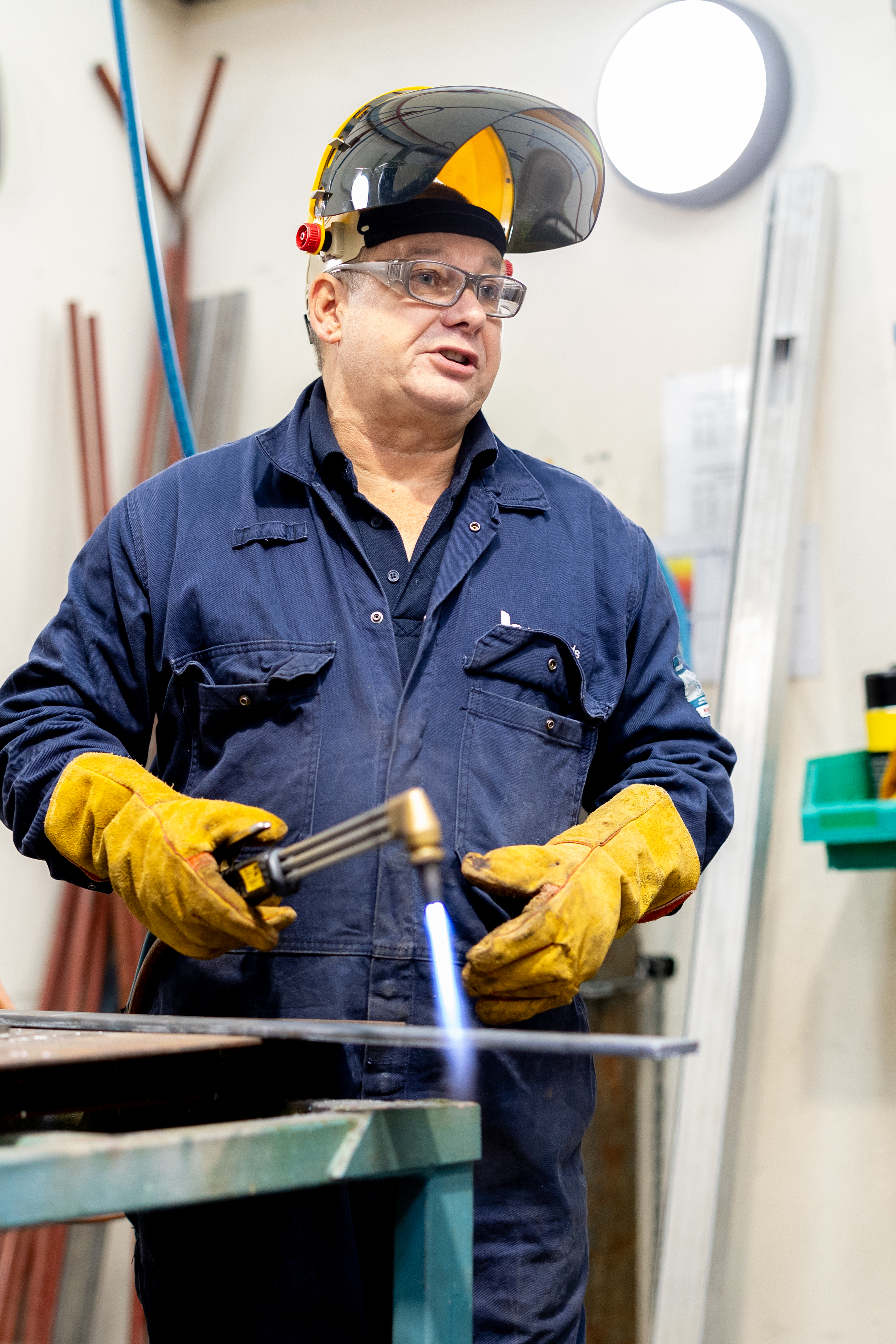 Welding student at Highlands College using a torch with active flame in a workshop, wearing full protective gear including face shield and gloves.