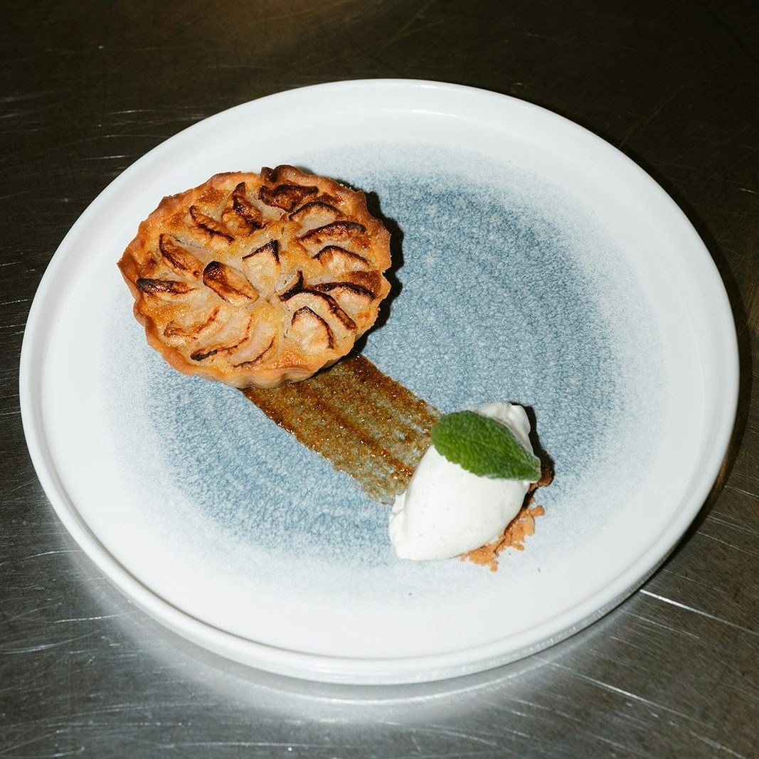A dessert on a circular plate It looks like a small apple pie with a quenelle shaped white ice cream