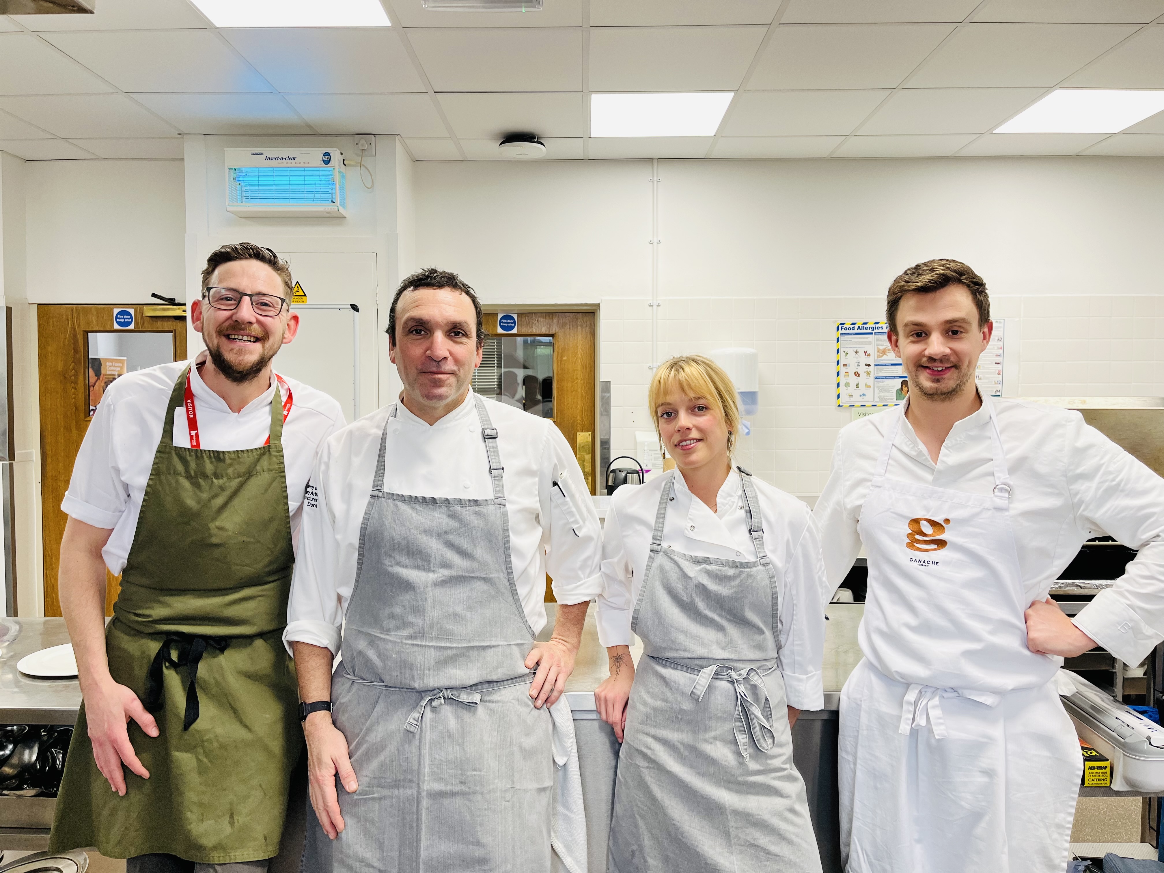 Culinary arts students at Highlands College standing in a professional kitchen wearing chef uniforms, surrounded by commercial cooking equipment.