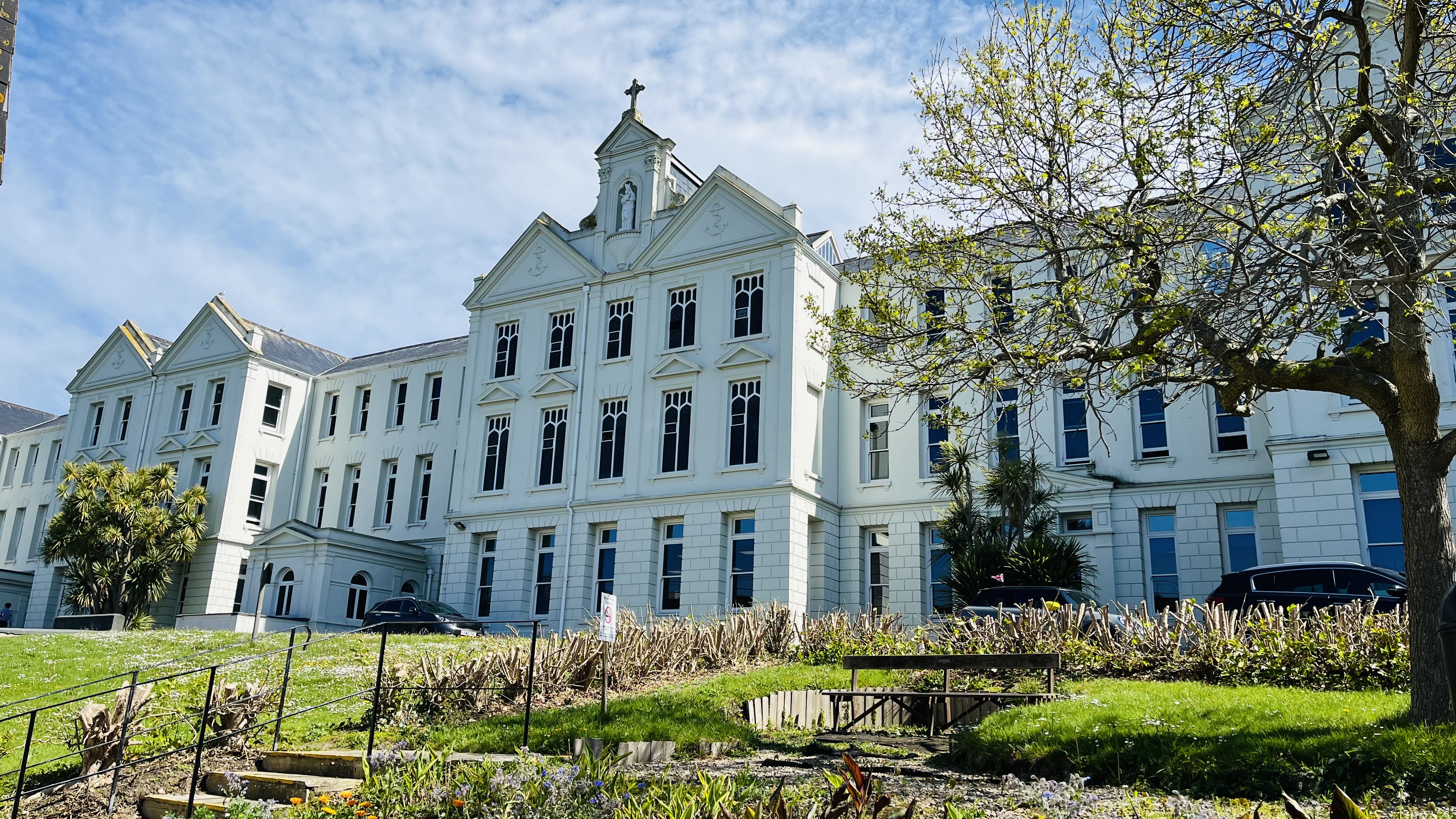 Highlands College's Turner building with classical architecture and a central tower, surrounded by grass, trees, benches, and pathways under a partly cloudy sky.