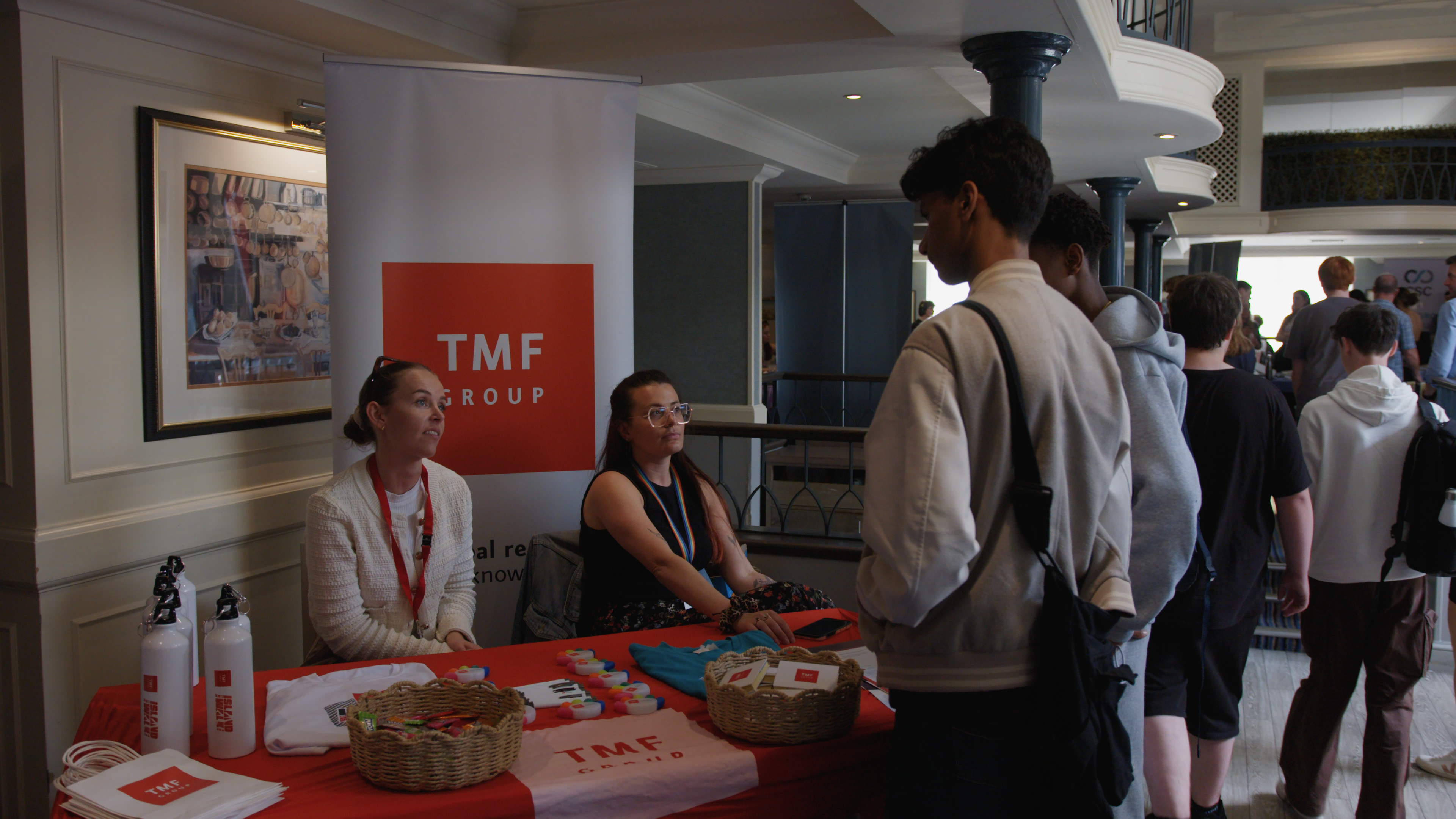 A photo of 2 ladies from TMF group at a recruitment fair chatting to a pair of young male students.