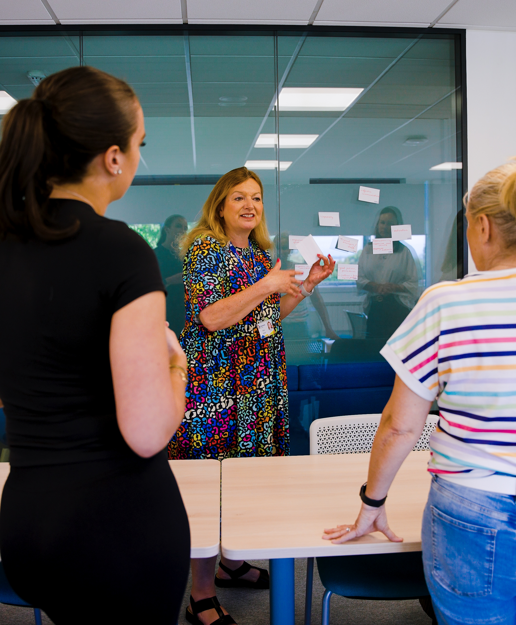 Teacher talking to two adult female students in the classroom, teacher is facing the camera and students are looking at her.