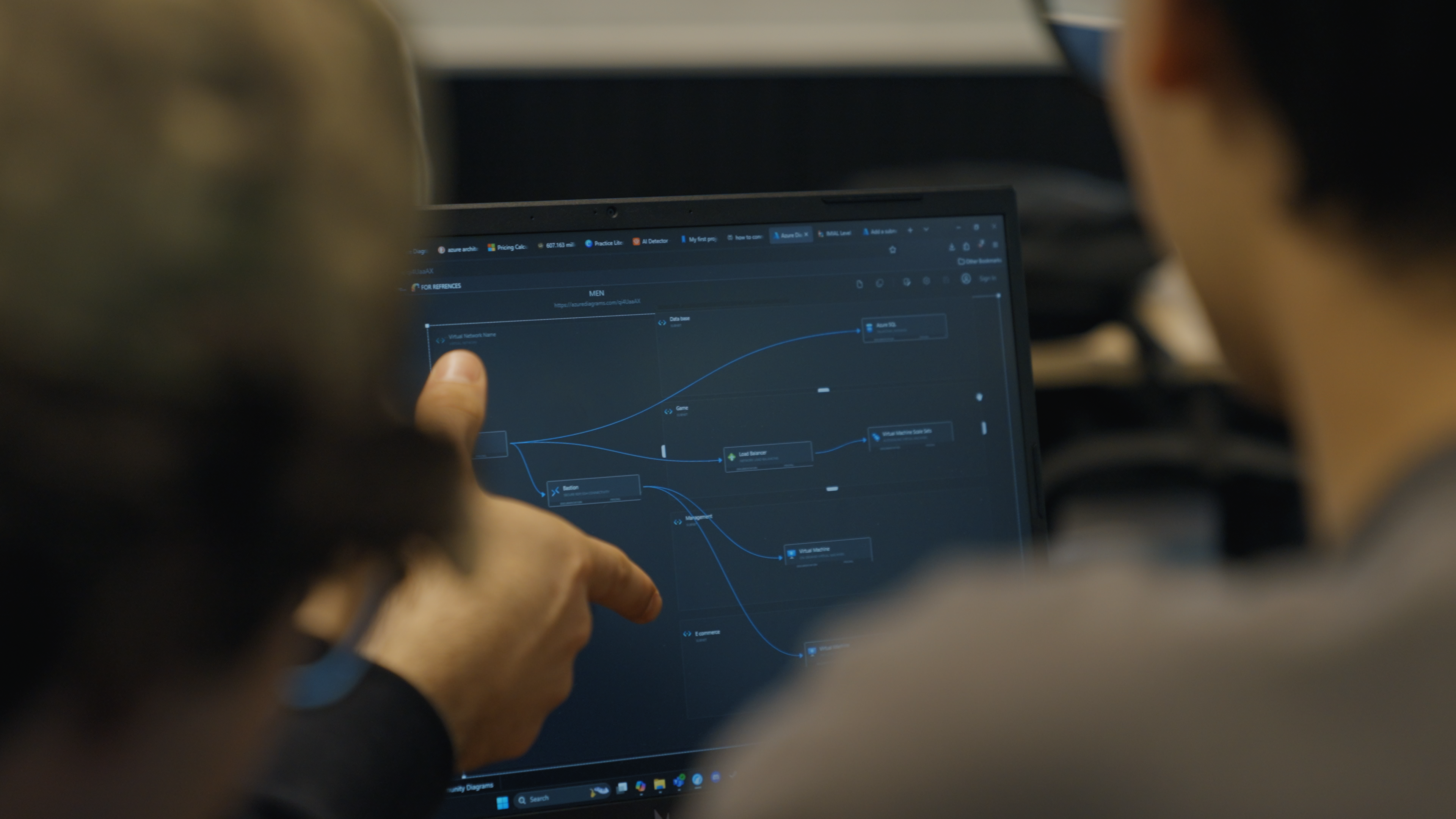 A close-up shot of two individuals from behind looking at a laptop screen. One of the individuals points towards the screen.