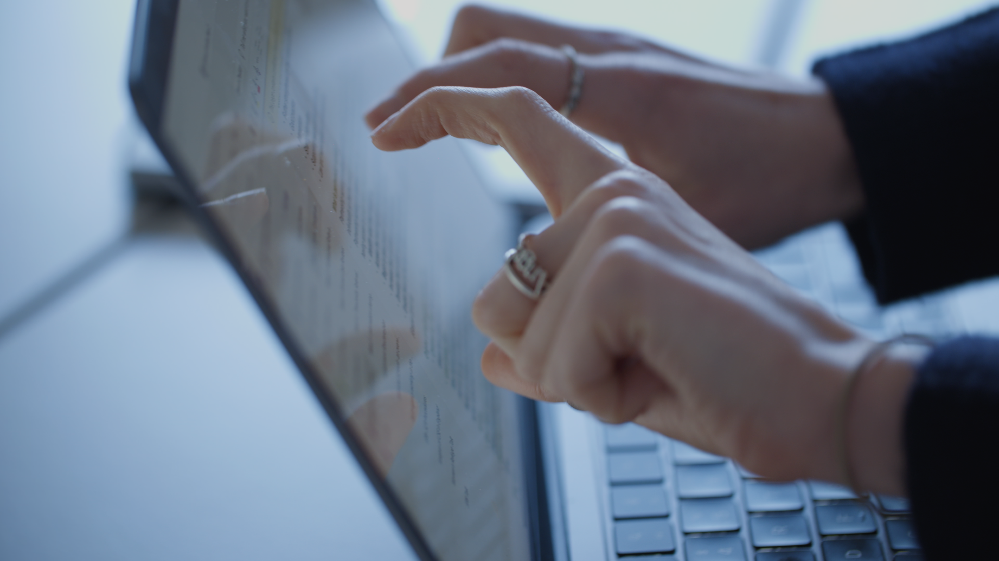 A medium close-up of two hands about to touch the screen of a laptop covered in text.