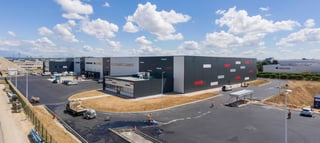 Vue aérienne de l'entrepôt logistique Montea à Meyzieu, France avec accents rouges et une cour fraîchement asphaltée en travaux