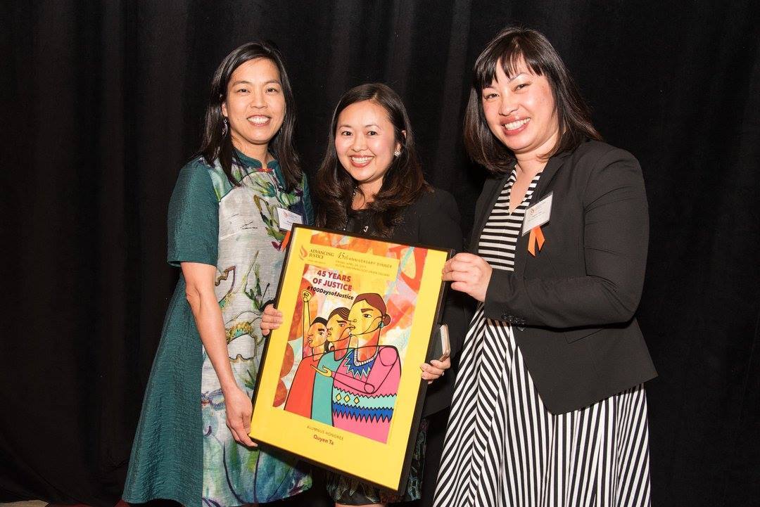 Three women hold up a poster in front of a black background